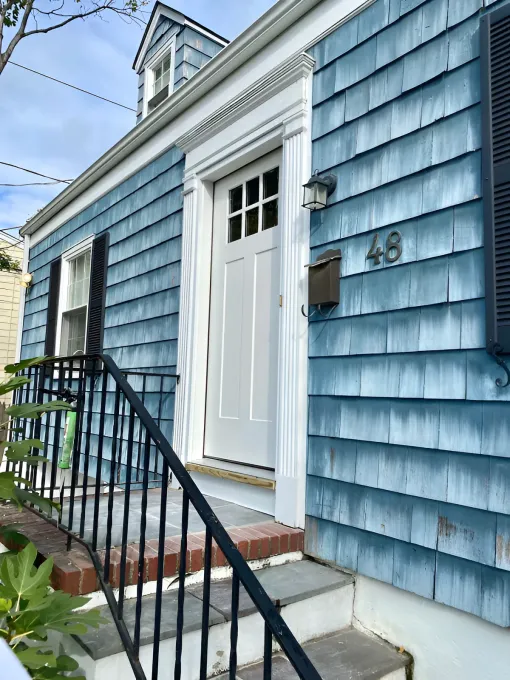 Blue shingled house with white door, black shutters, and wrought iron railing. Number 49 is on the mailbox.