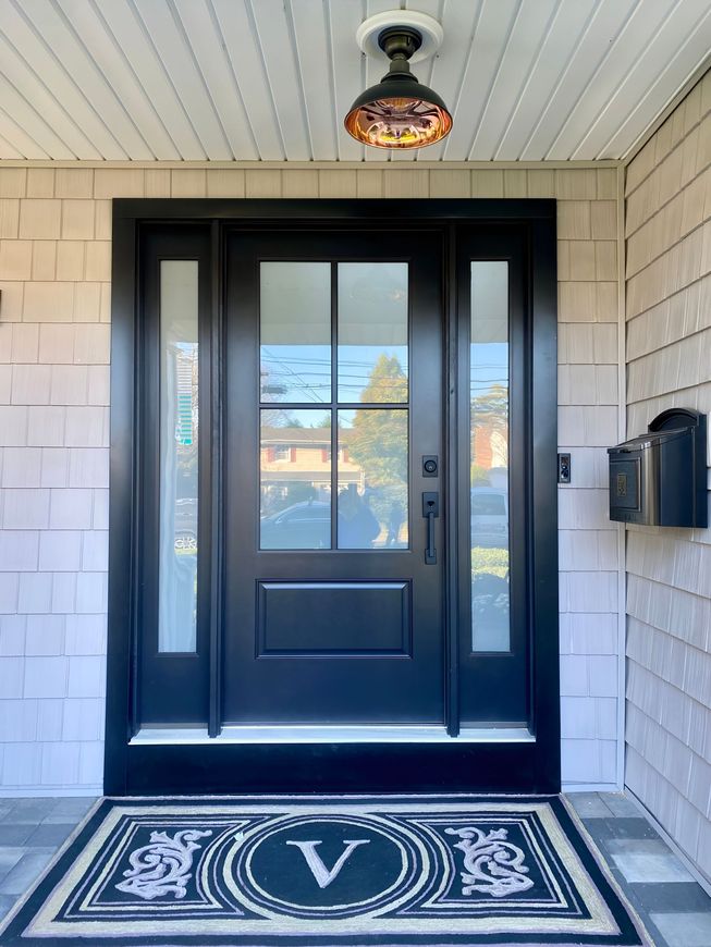 Black front door with sidelights, welcome mat, and decorative light fixture.