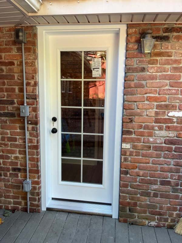 White-framed glass door on a brick wall exterior. Two electrical boxes and a wall sconce are visible.