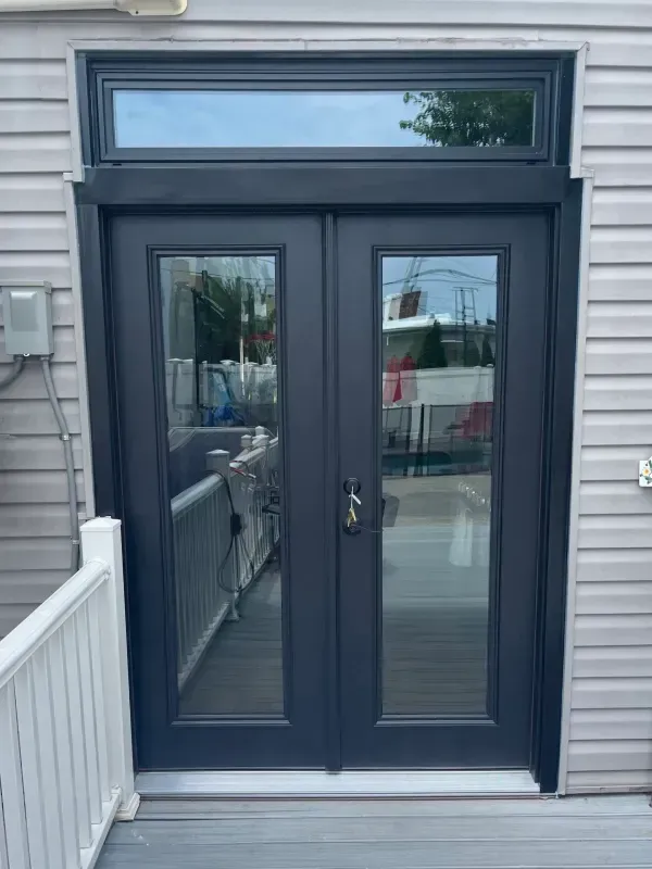 Black double doors with glass panels and a transom window. Set in a gray siding exterior.