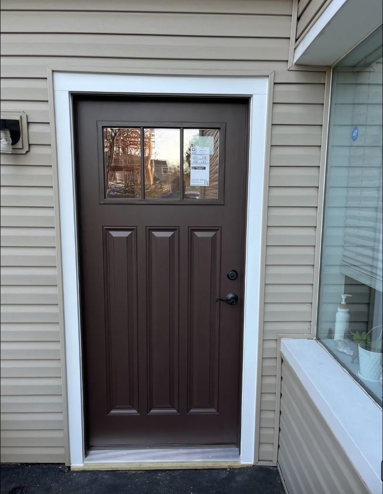Brown door with glass panel, white trim, on a beige siding house.