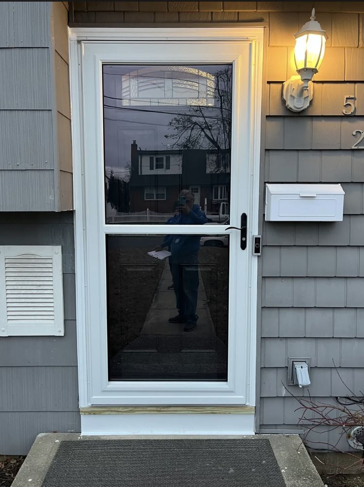 White screen door with a person reflected in the glass, set in a gray house with a light and mailbox.