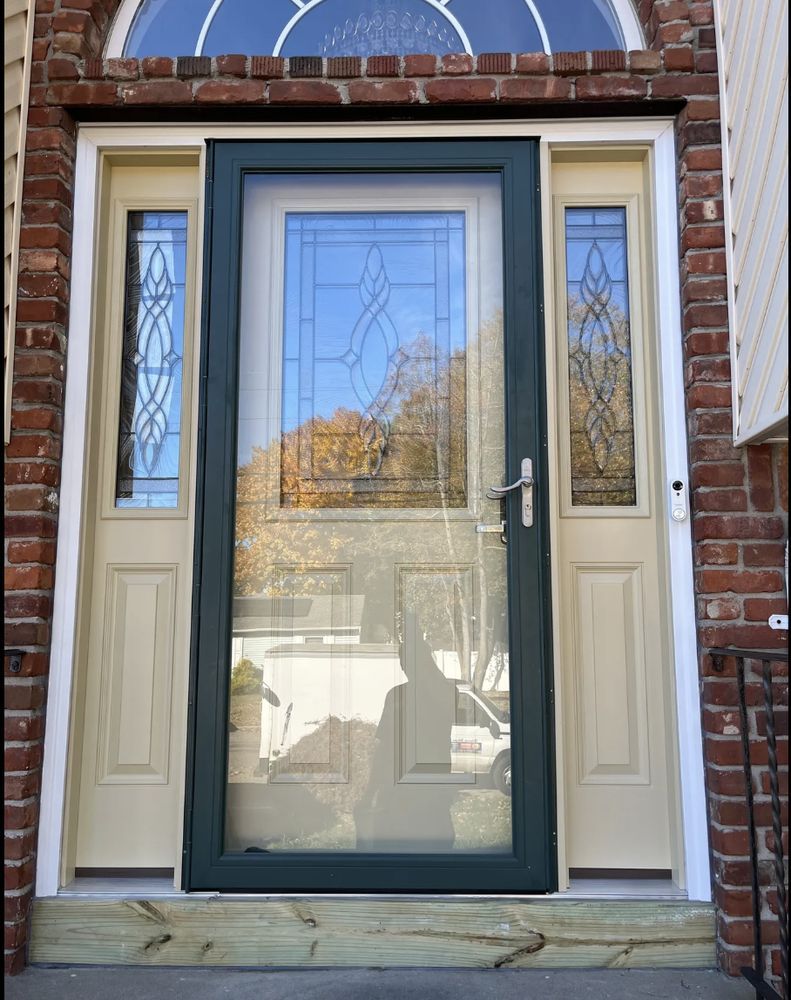 Exterior view of a front door with sidelights. Green screen door, tan door frame, and brick exterior.
