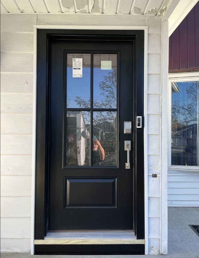 Black front door with glass panes and a handle. White siding surrounds the doorframe.