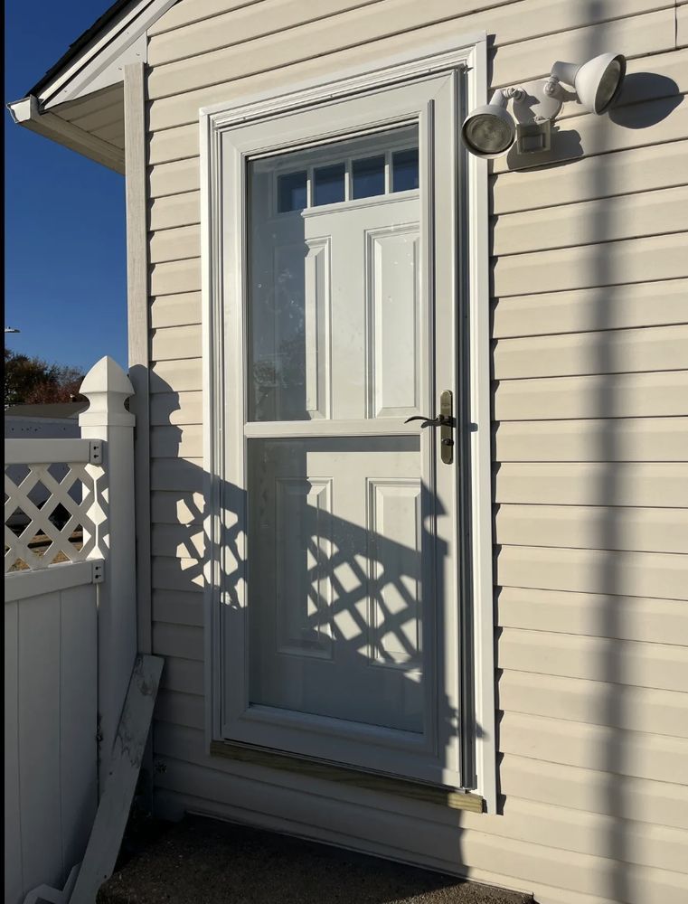 White exterior door with a screen, set in a light beige siding, lit by a nearby spotlight.