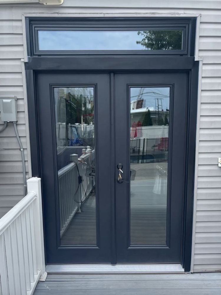 Black double doors with glass panels and a transom window on a gray building.