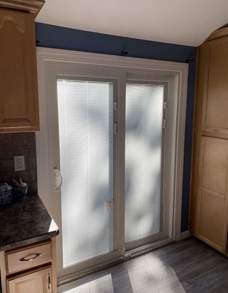 Sliding glass door with blinds in a kitchen. Blue wall, white trim, and wood cabinets.