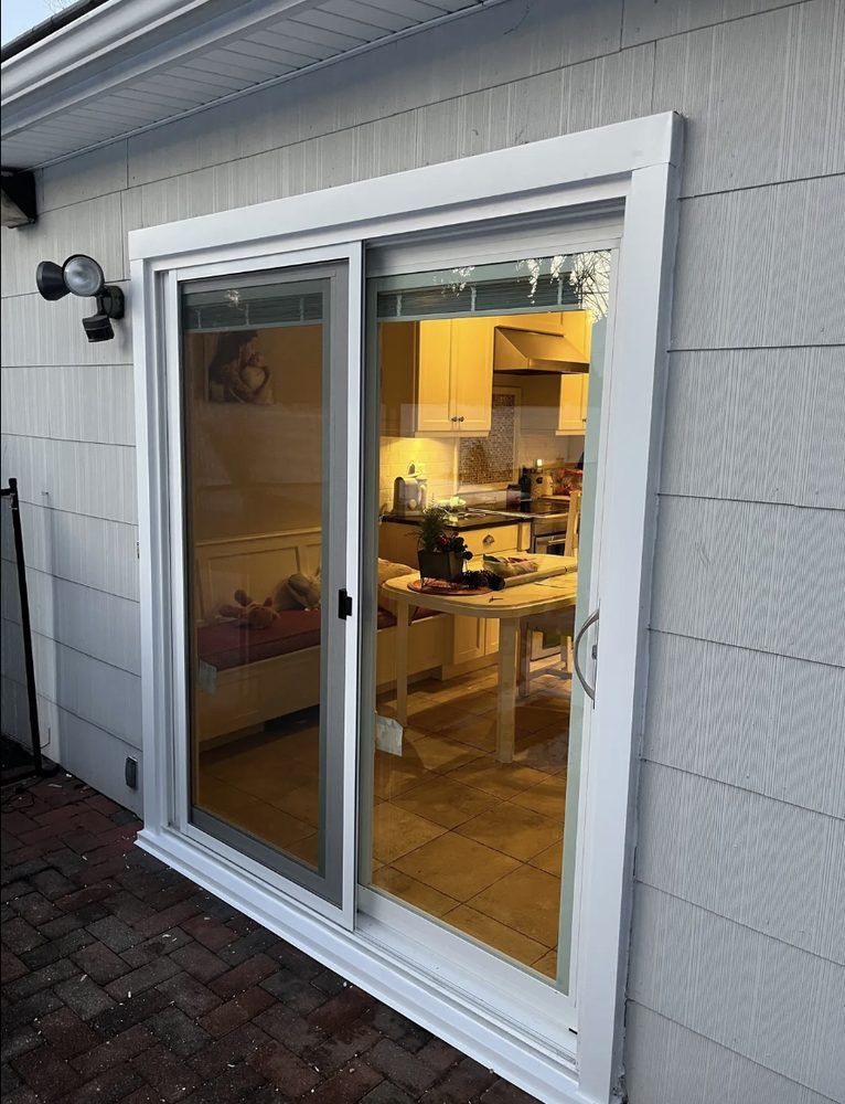 White sliding glass door on a white house exterior, with a view into a kitchen.