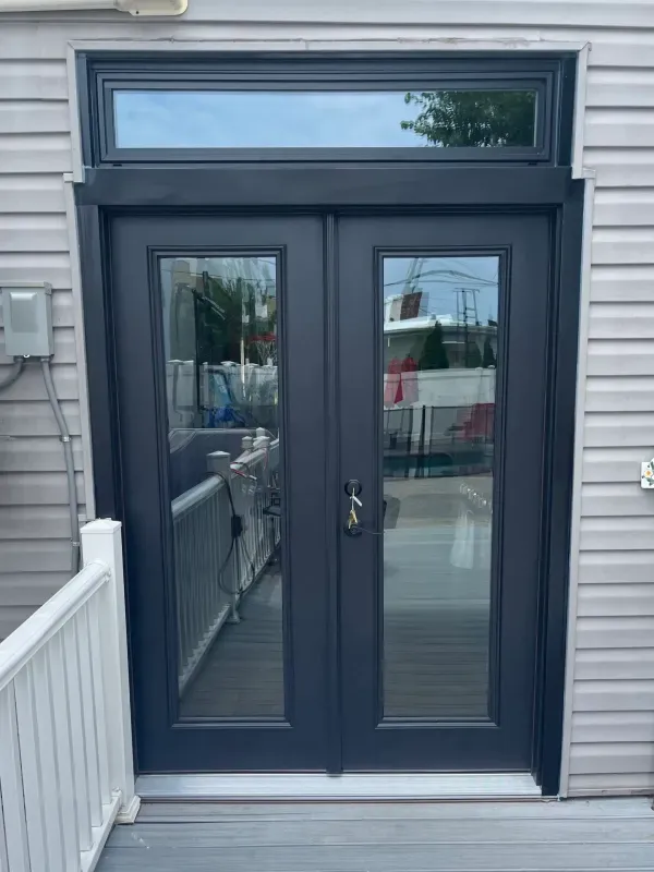 Dark blue double glass front doors with a transom window and white railing on a house entry.