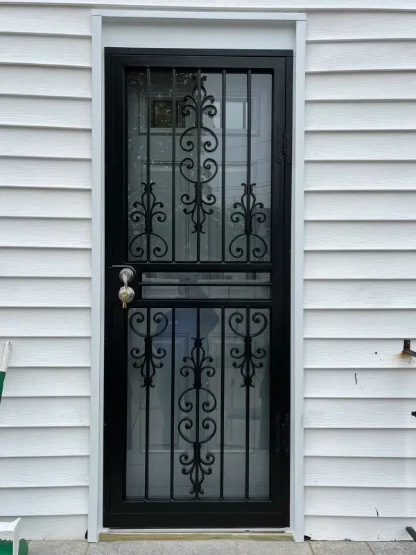 Black security door with decorative wrought-iron bars set in white vinyl siding.