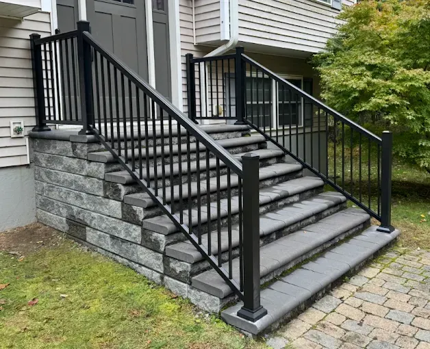 Black metal stair railings on gray stone steps leading to a house entrance.