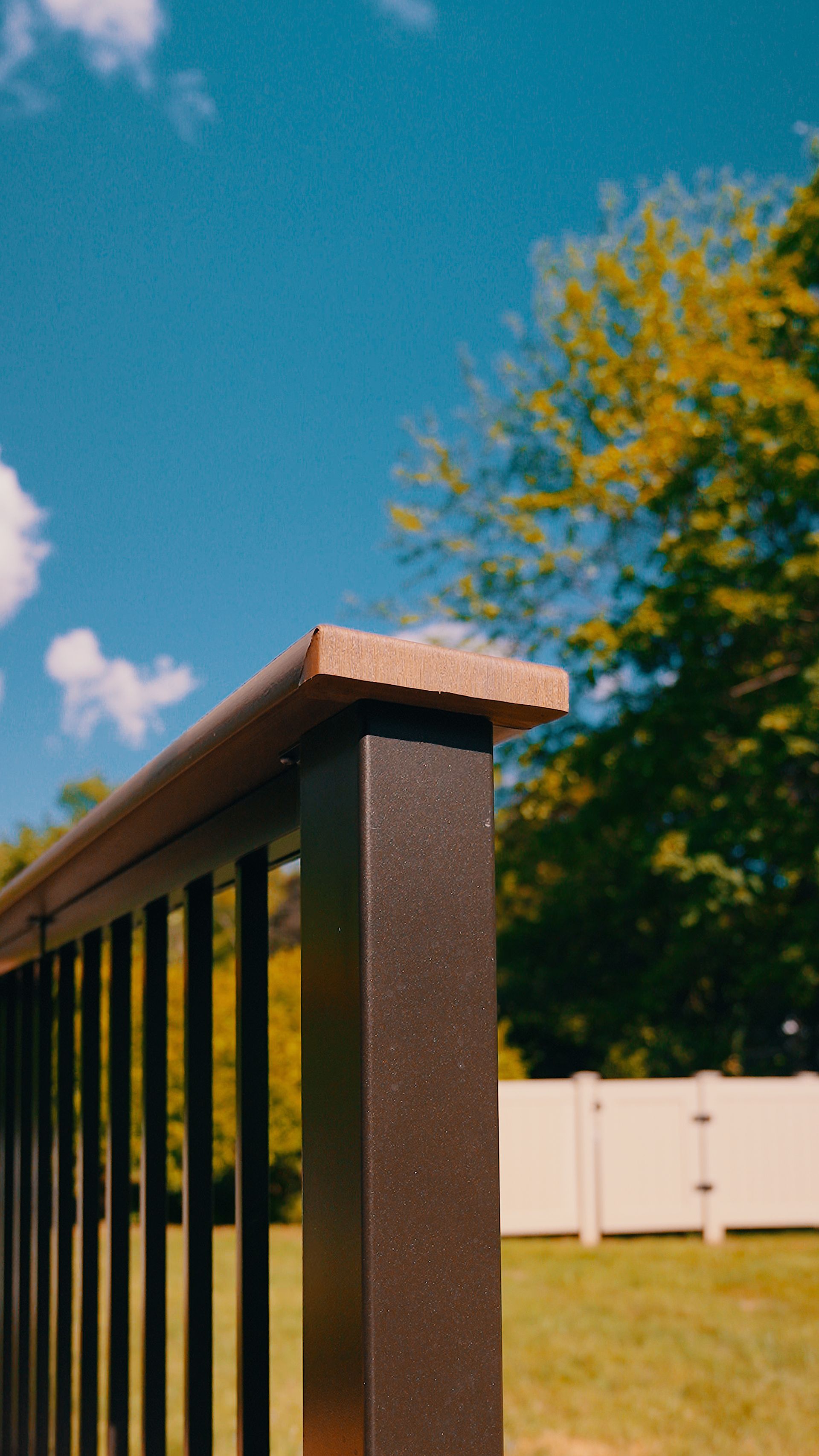 A close up of a railing with a white fence in the background.