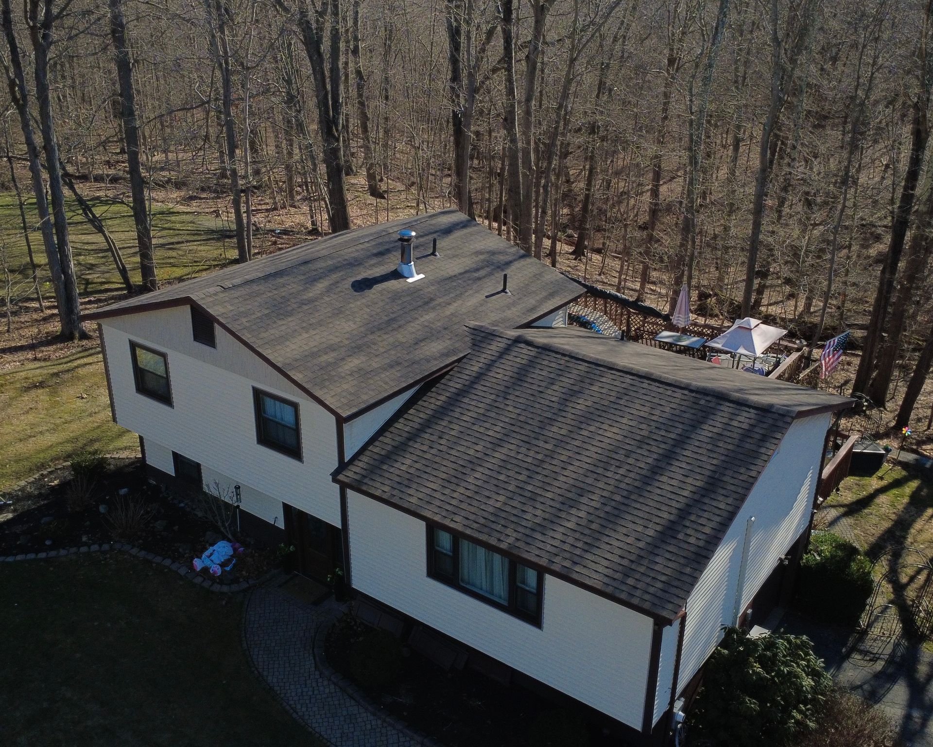 Aerial view of a white house with a dark roof surrounded by leafless trees.