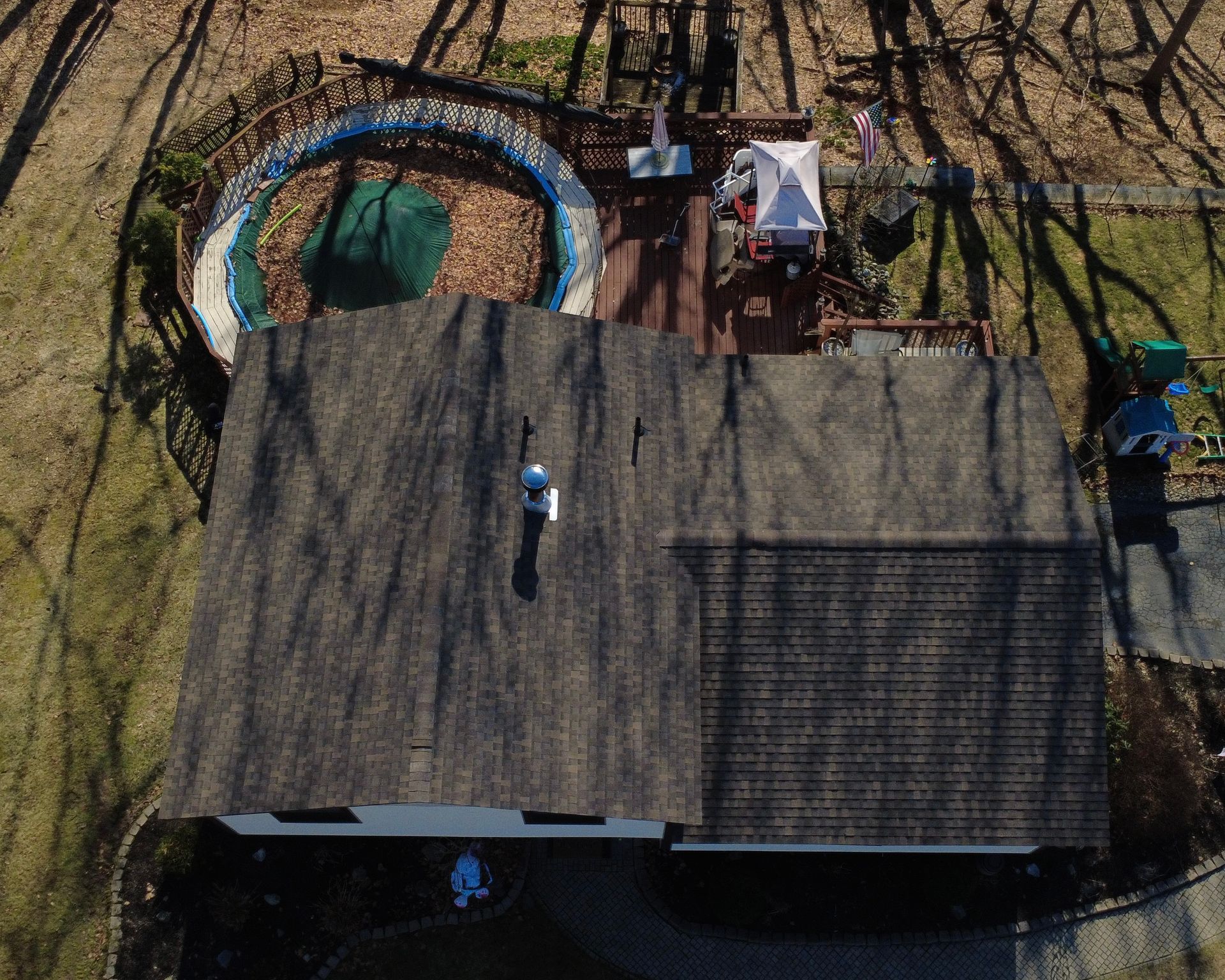 Overhead view of a rooftop with a person standing near a circular pool and patio chairs in a wooded yard