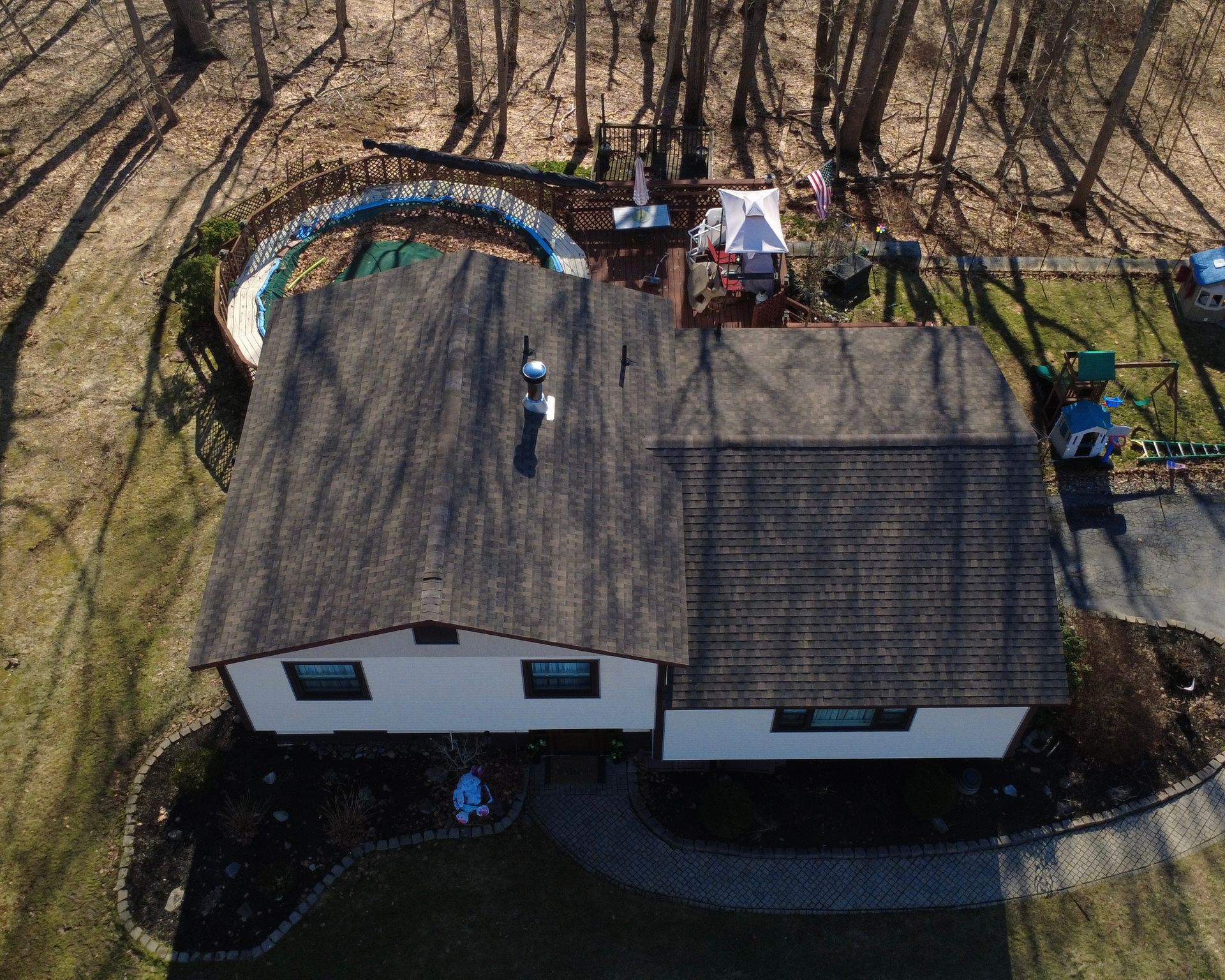 Aerial view of a house with a dark roof, surrounded by leafless trees and a yard with a small play area.
