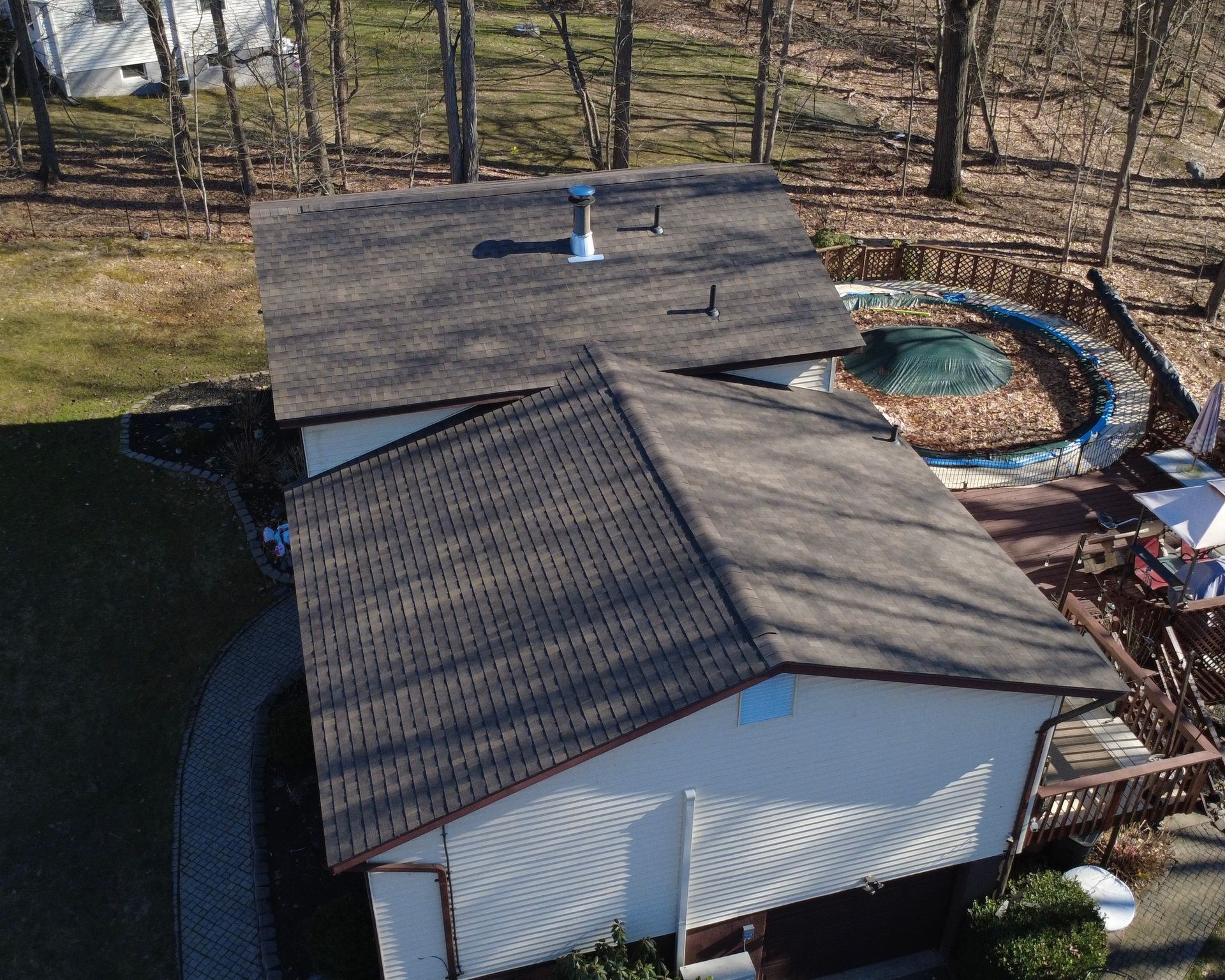 Aerial view of a shed roof with a chimney, surrounded by trees and a backyard pond.