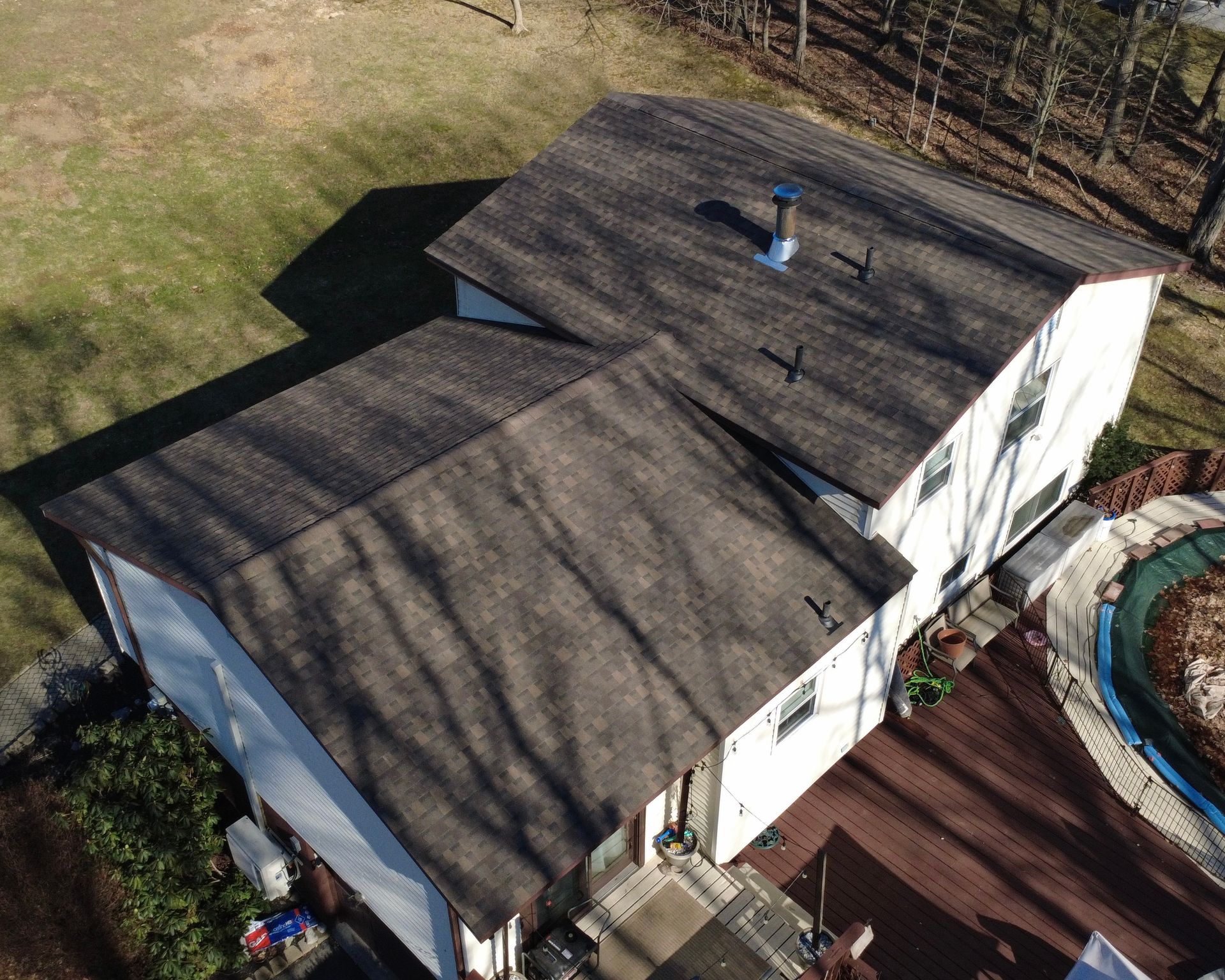 Aerial view of a white house with a dark roof beside a deck and round pool.
