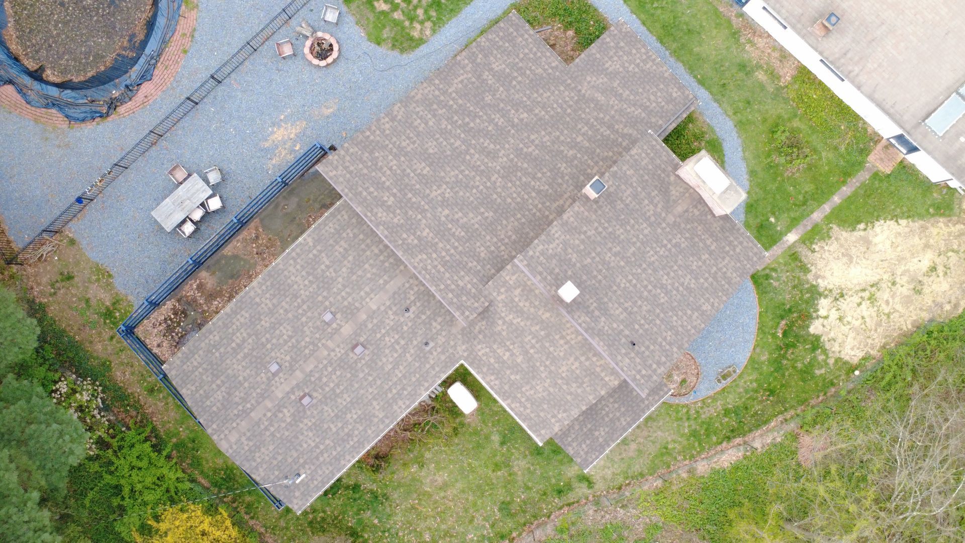Aerial view of a gray-roofed house with a yard, patio furniture, and green grass around it