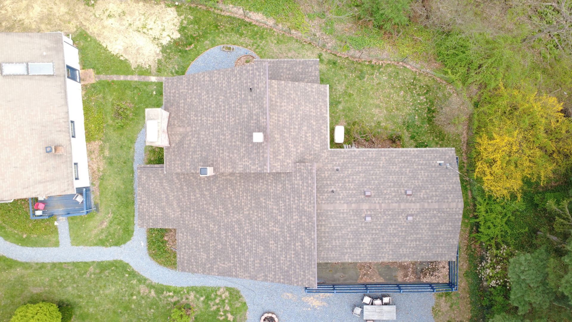Aerial view of a gray-roofed house with lawn, driveway, and trees around it.