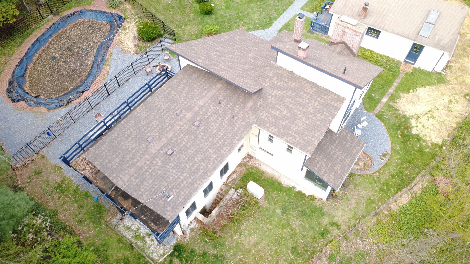 Aerial view of a large house with a fenced deck and small pond in a grassy yard.