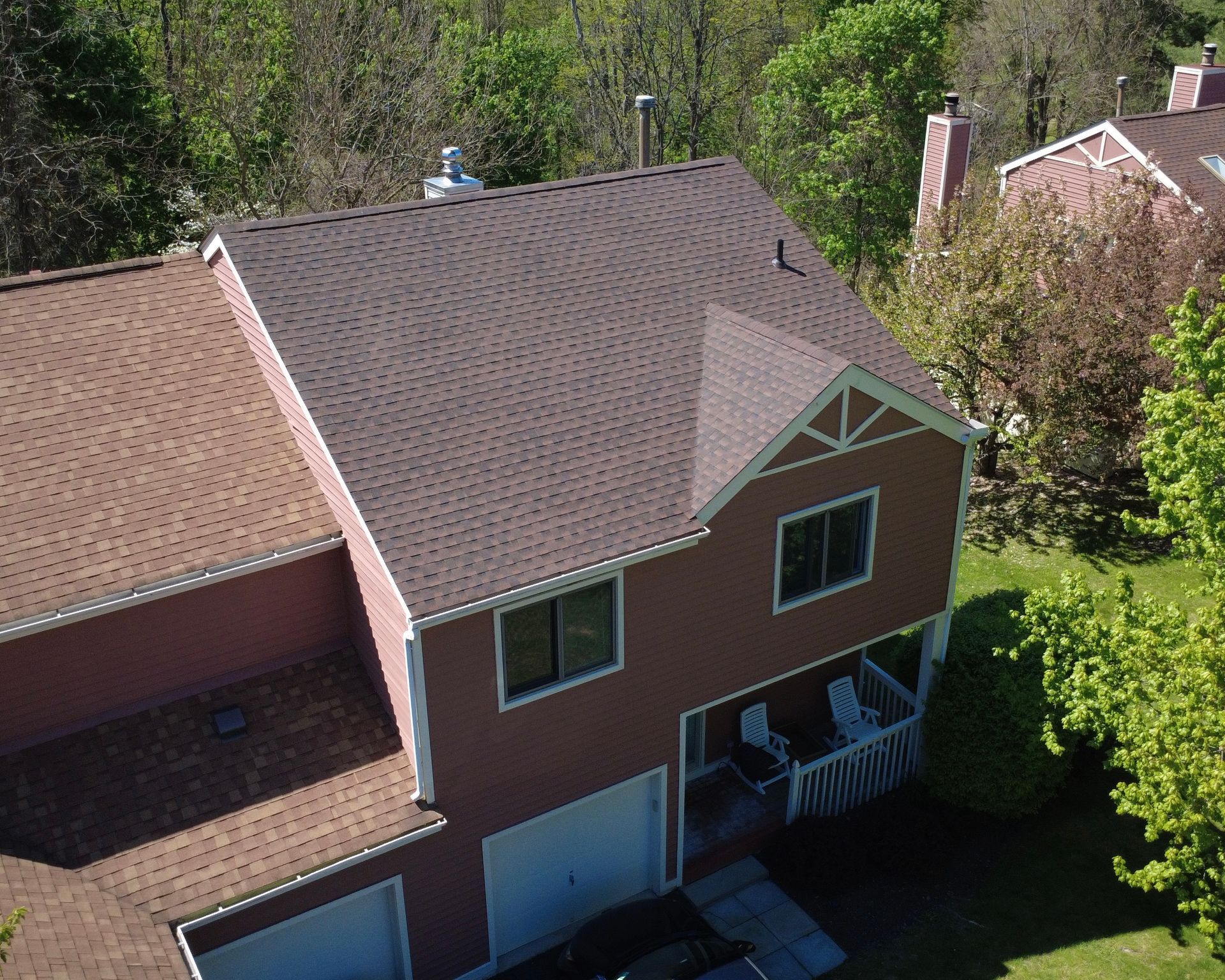 Aerial view of a brown two-story house with a dark roof, garage, and small front porch surrounded by trees.