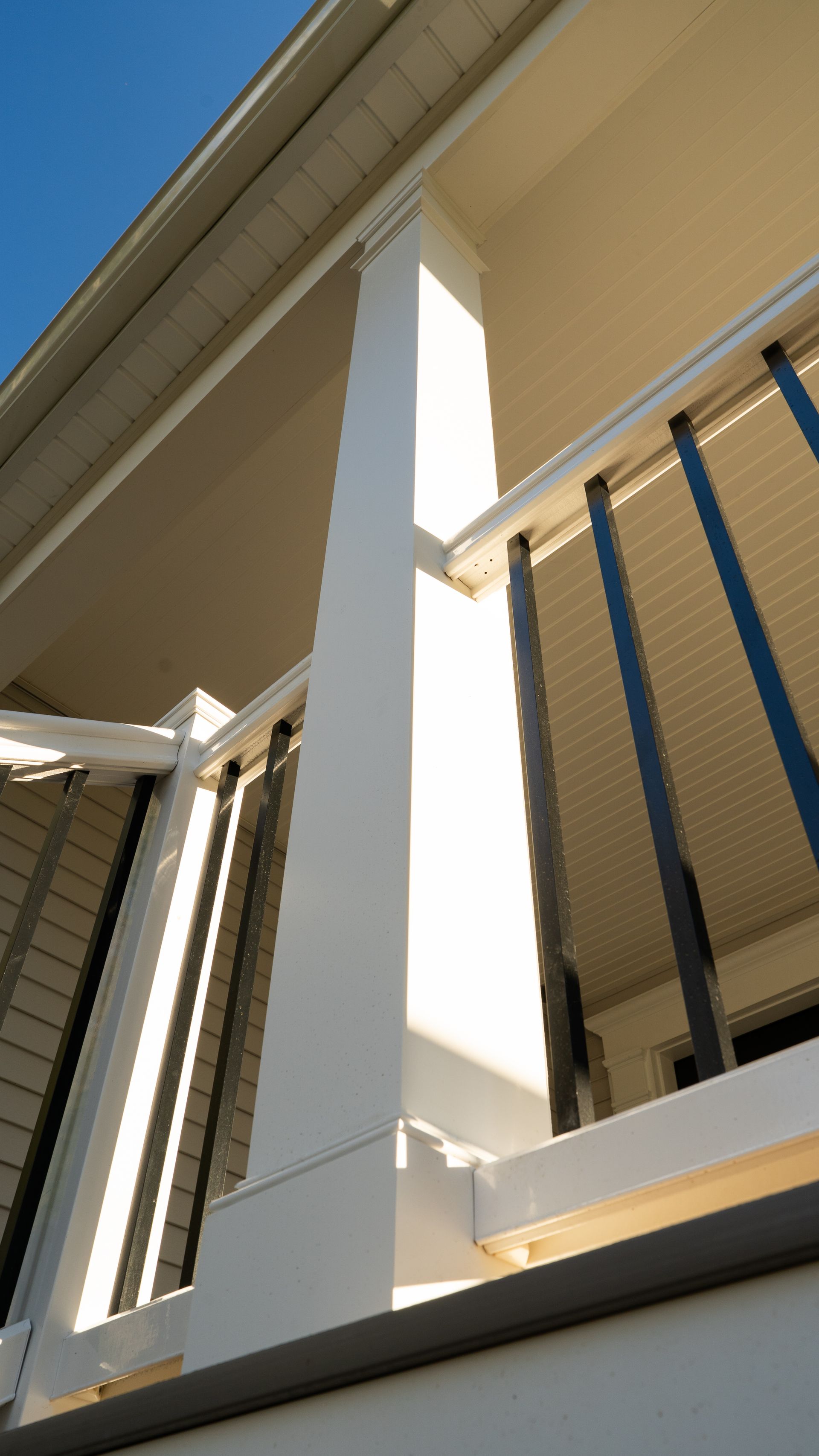 White porch column and beige house exterior with blue railings viewed from below
