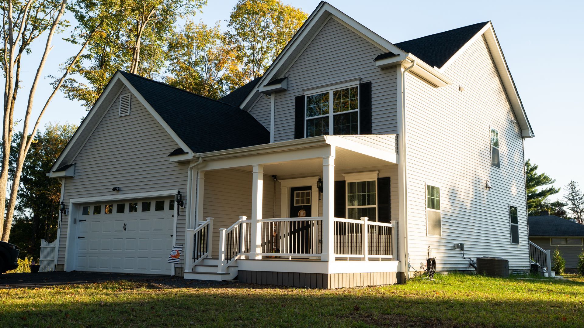 White two-story suburban house with black shutters, front porch, and attached garage in a sunny yard