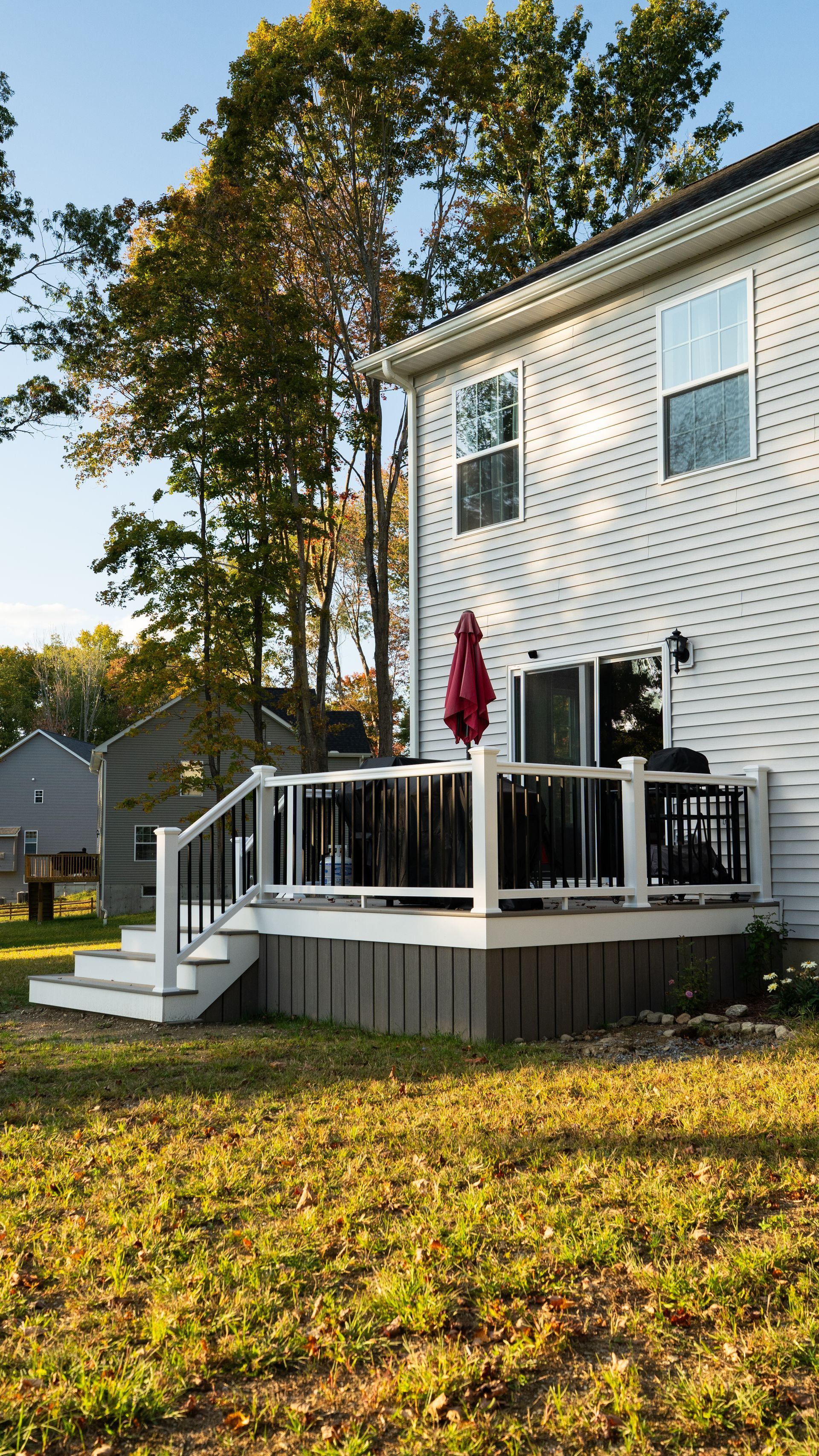 White two-story house with a front porch, red umbrella, and autumn trees in the yard