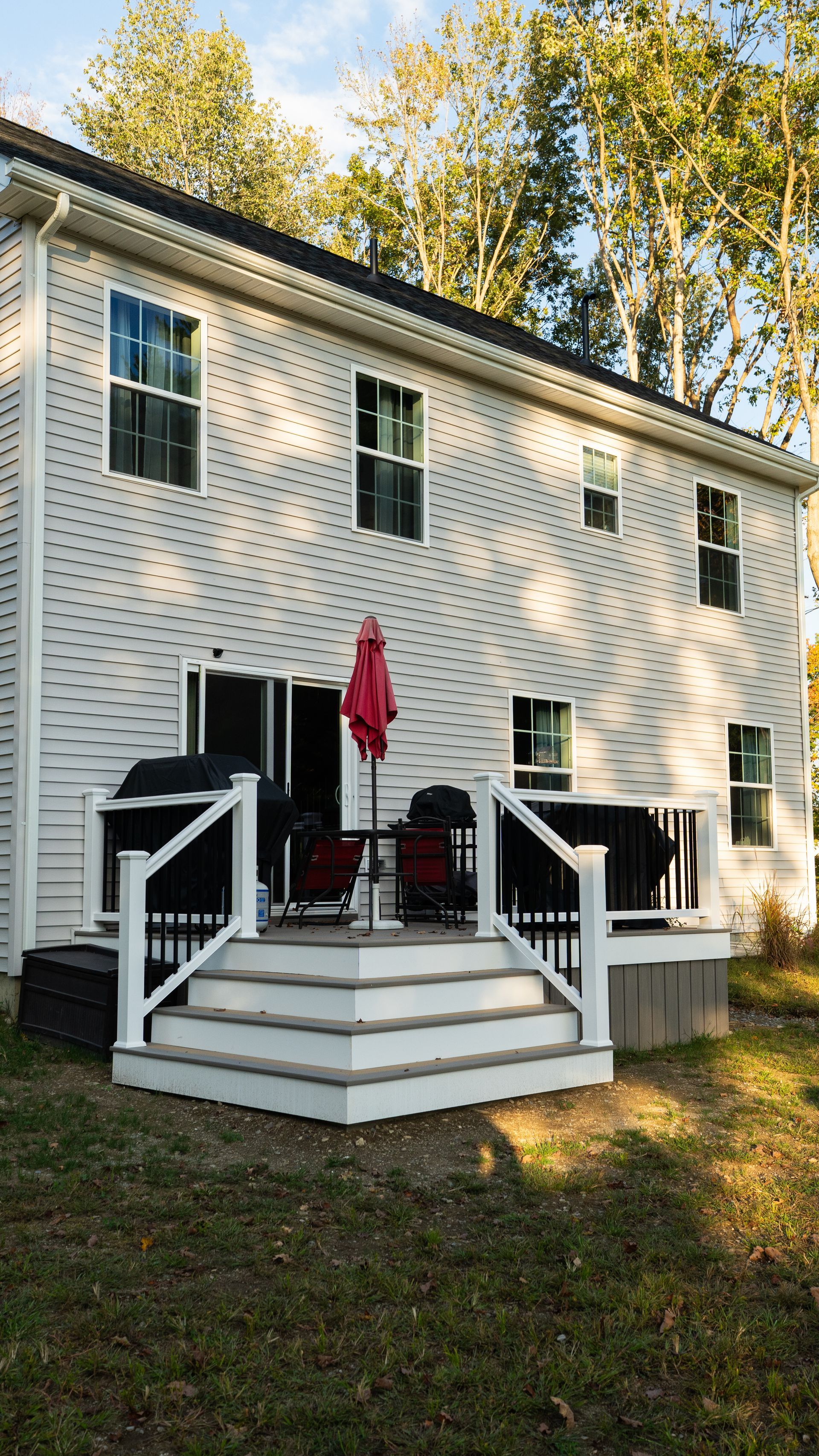 White house with a raised back deck and stairs, red umbrella, and autumn trees in the yard