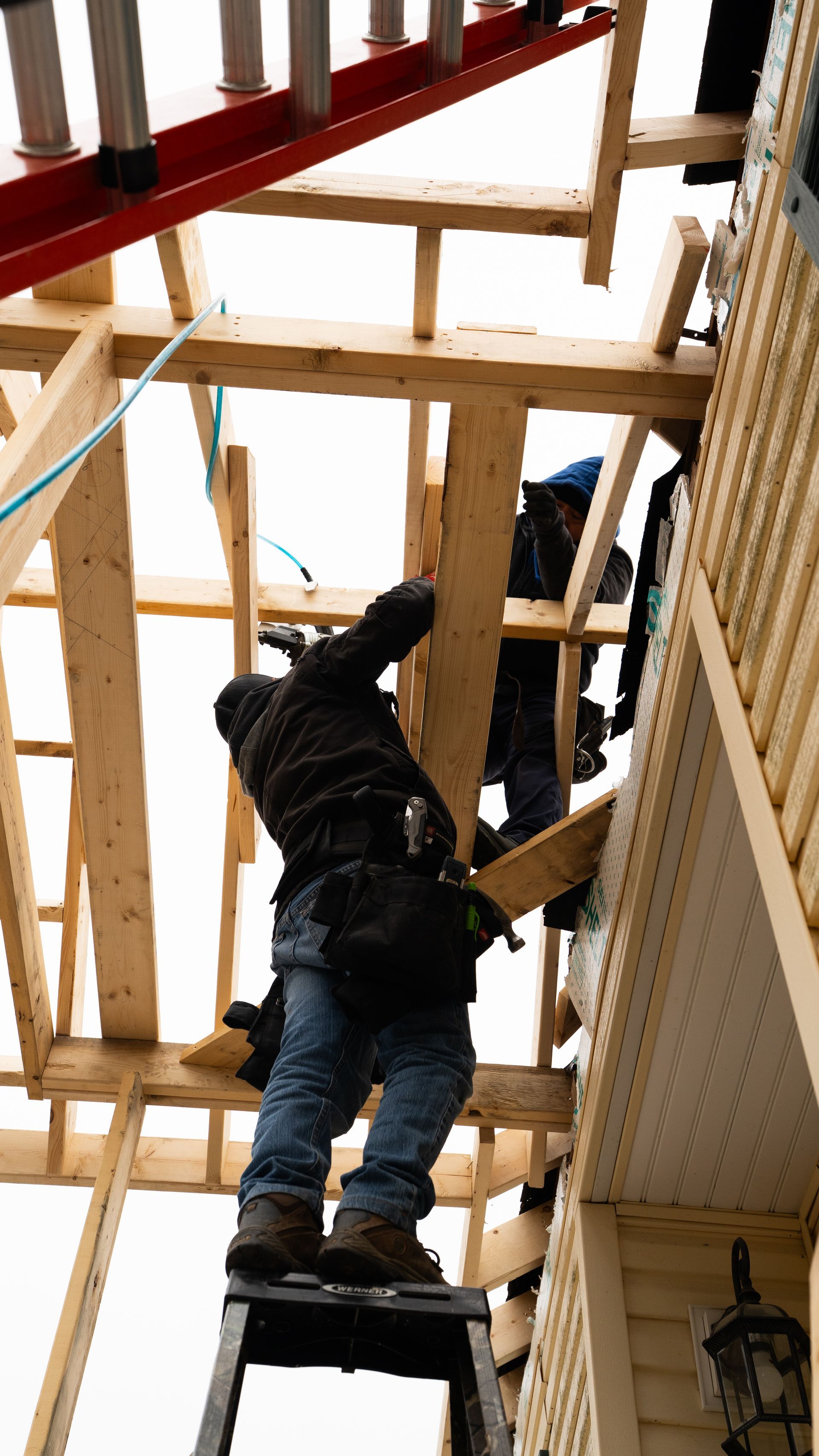Worker on a ladder framing a wooden structure at a construction site.