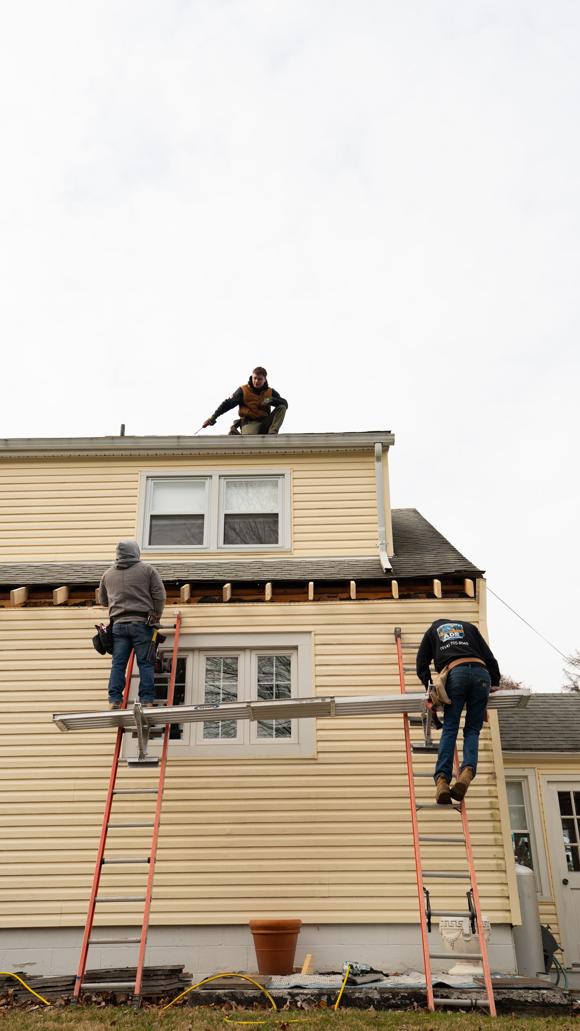 Workers on ladders repairing the roof and siding of a house under construction