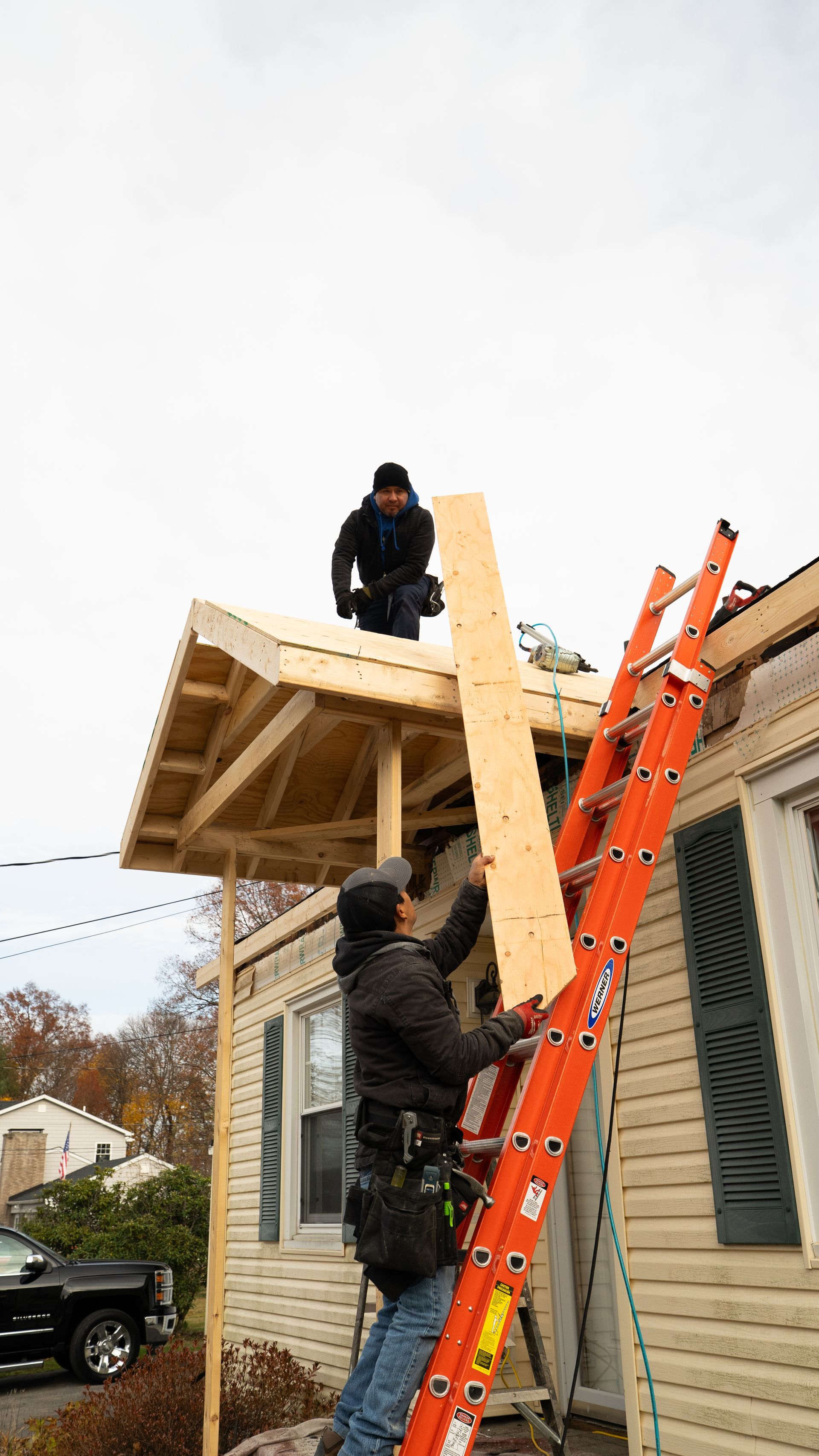 Two workers on ladders building a small roof extension on a house