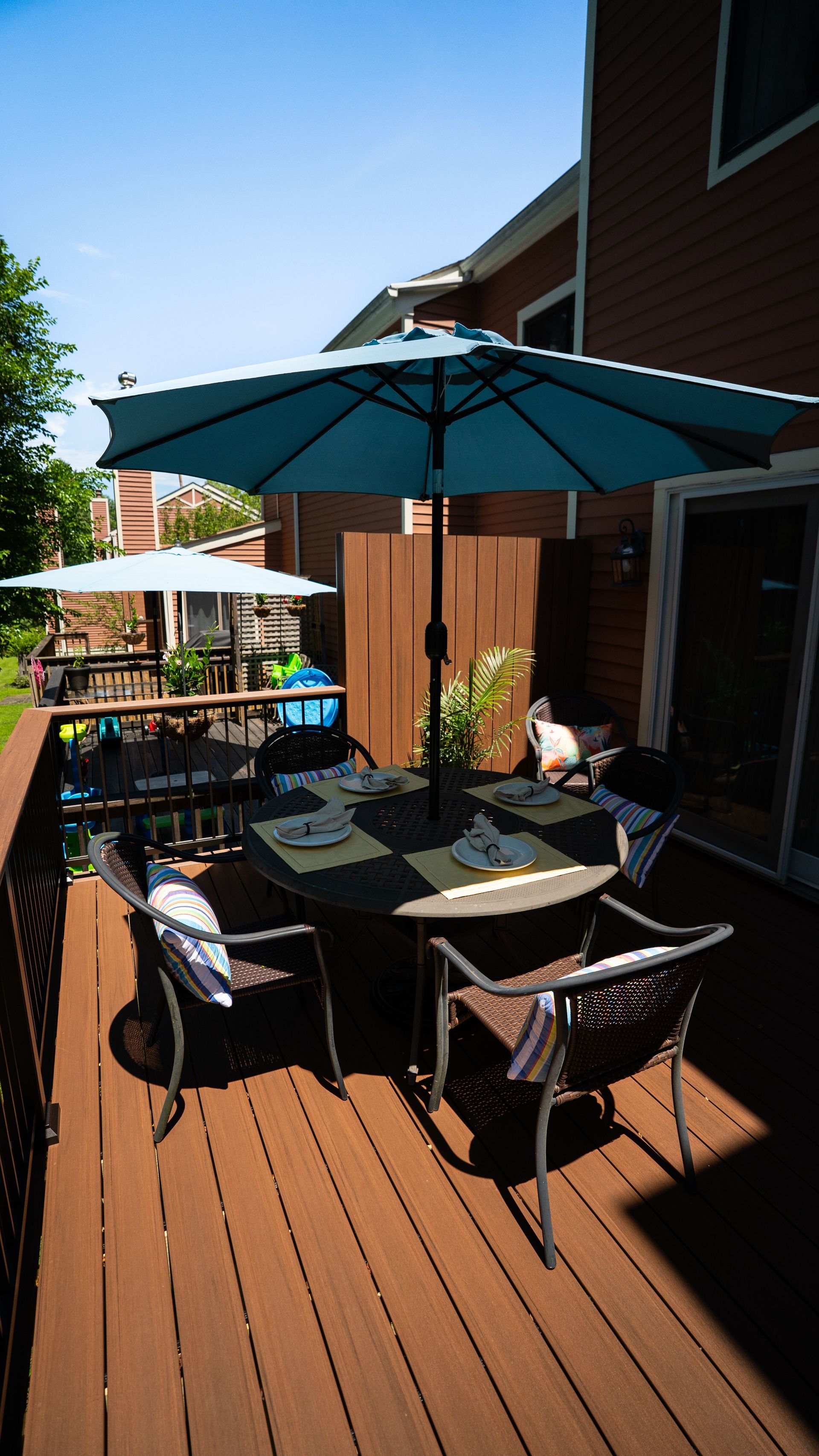 Wooden patio deck with outdoor table, chairs, and teal umbrellas beside a house