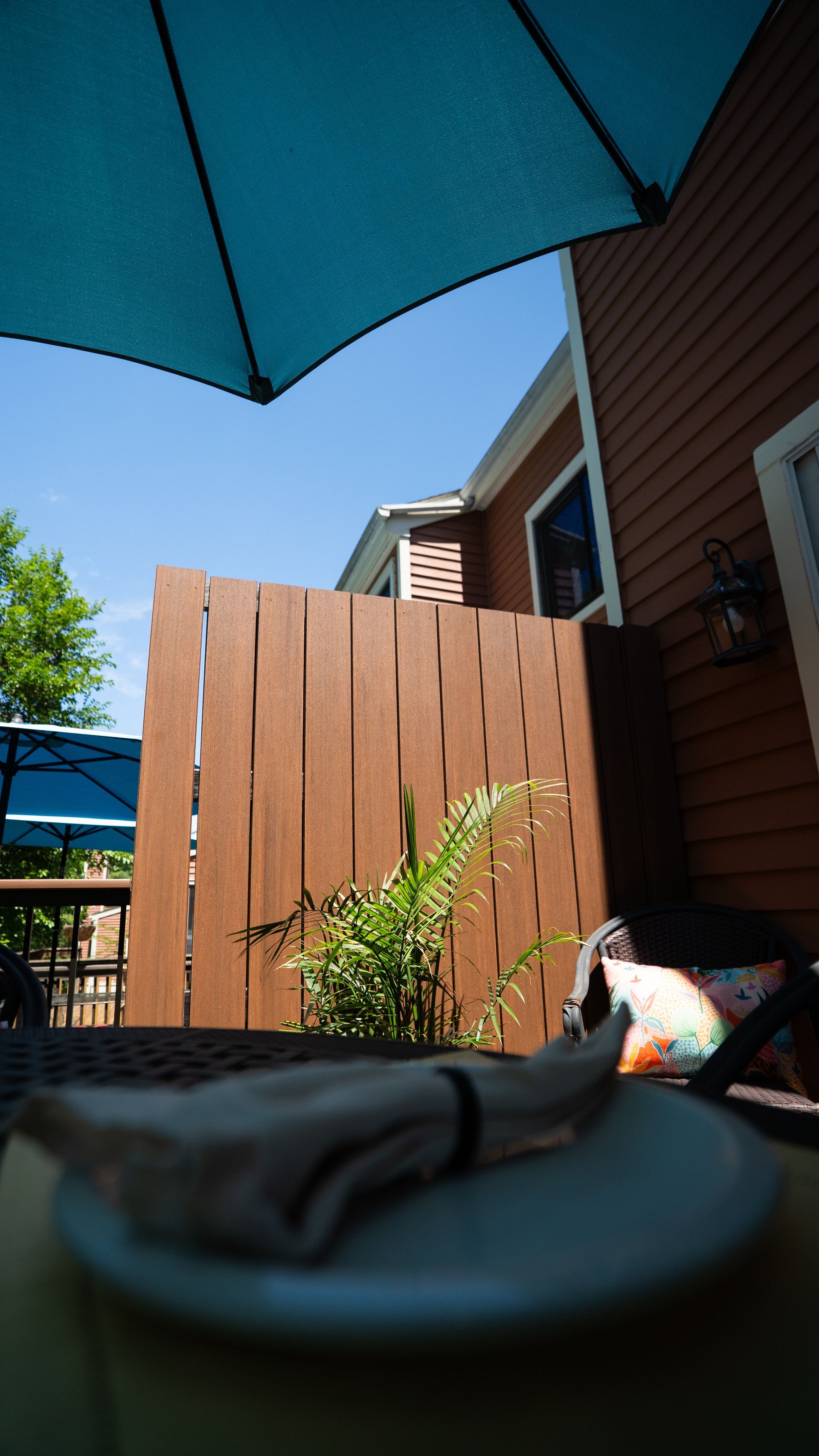 Umbrella-shaded patio with wooden fence, brown house siding, and a table in the foreground.