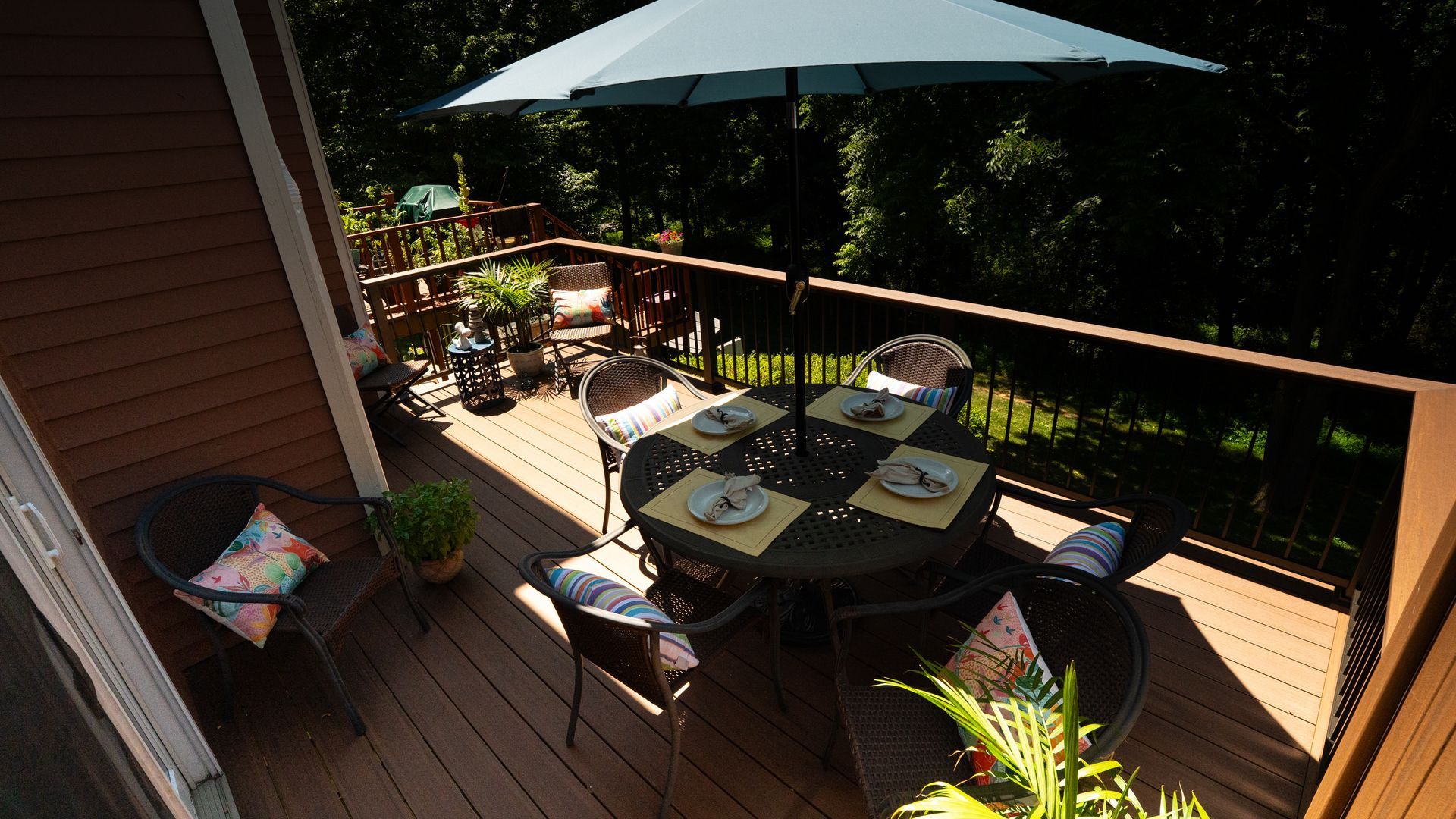 Patio deck with outdoor dining table, umbrella, chairs, and potted plants in sunlight