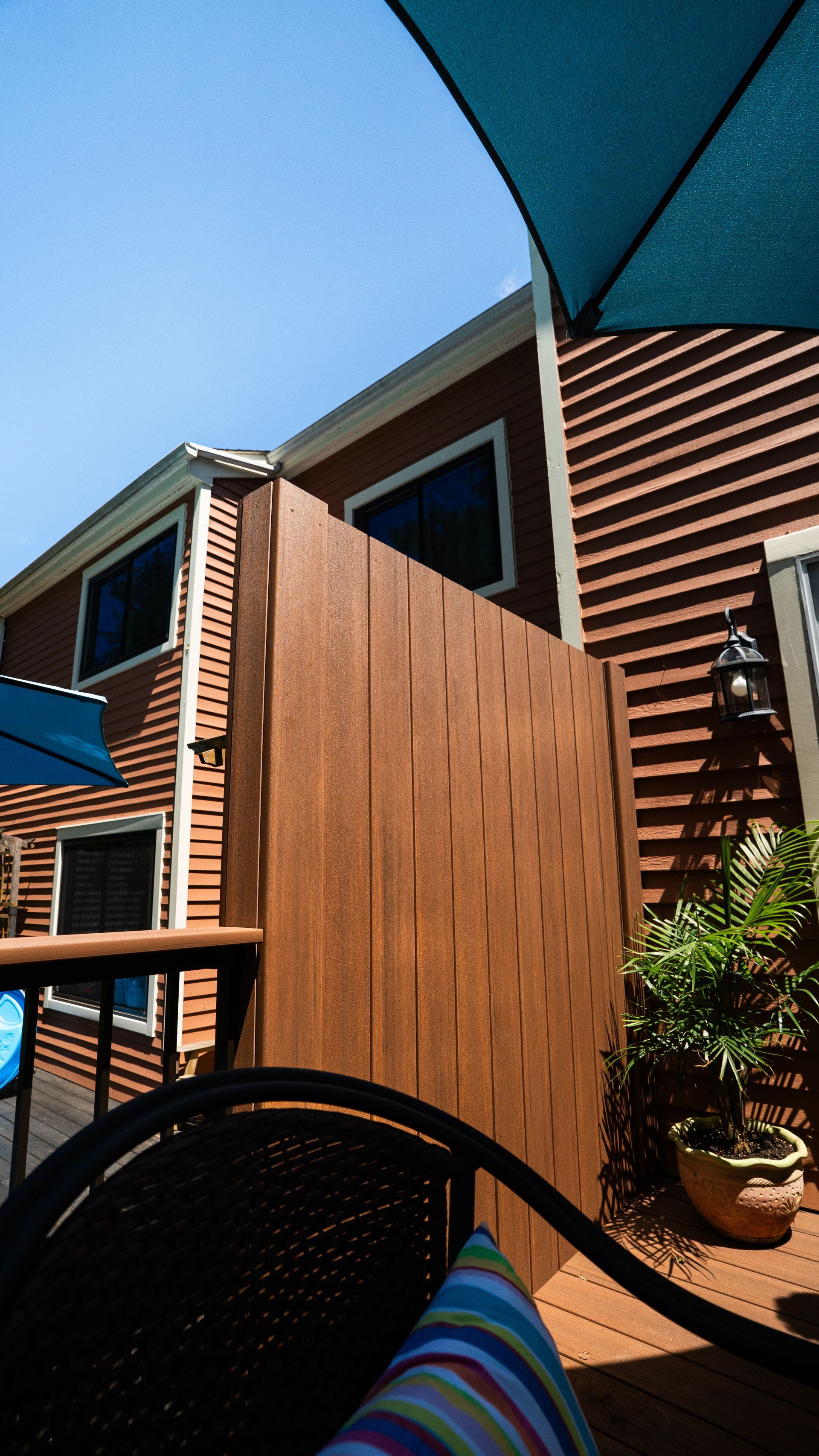 Outdoor patio with blue umbrella, striped chair, potted plant, and modern wood-sided building in sunlight