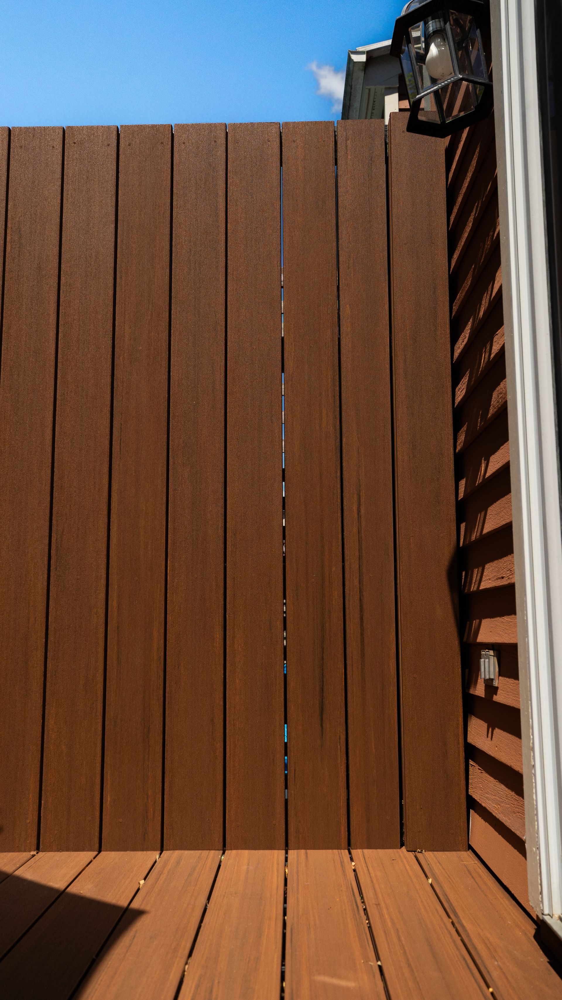 Brown wooden fence and deck against a blue sky, with a striped awning on the right