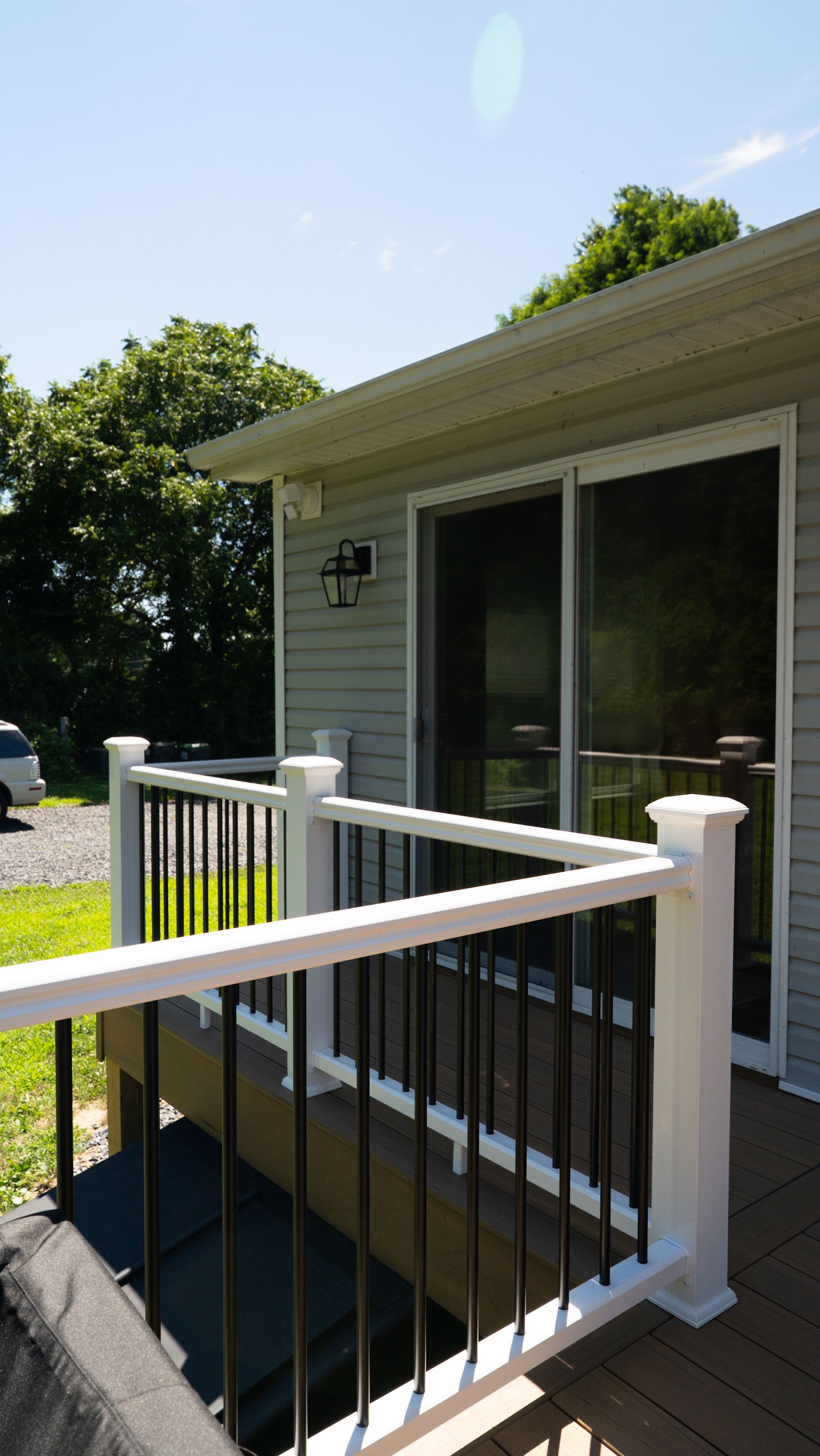 Front porch with white railing and sliding glass door on a sunny house exterior