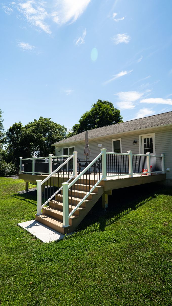 White porch with stairs and railing on a small house in a sunny grassy yard