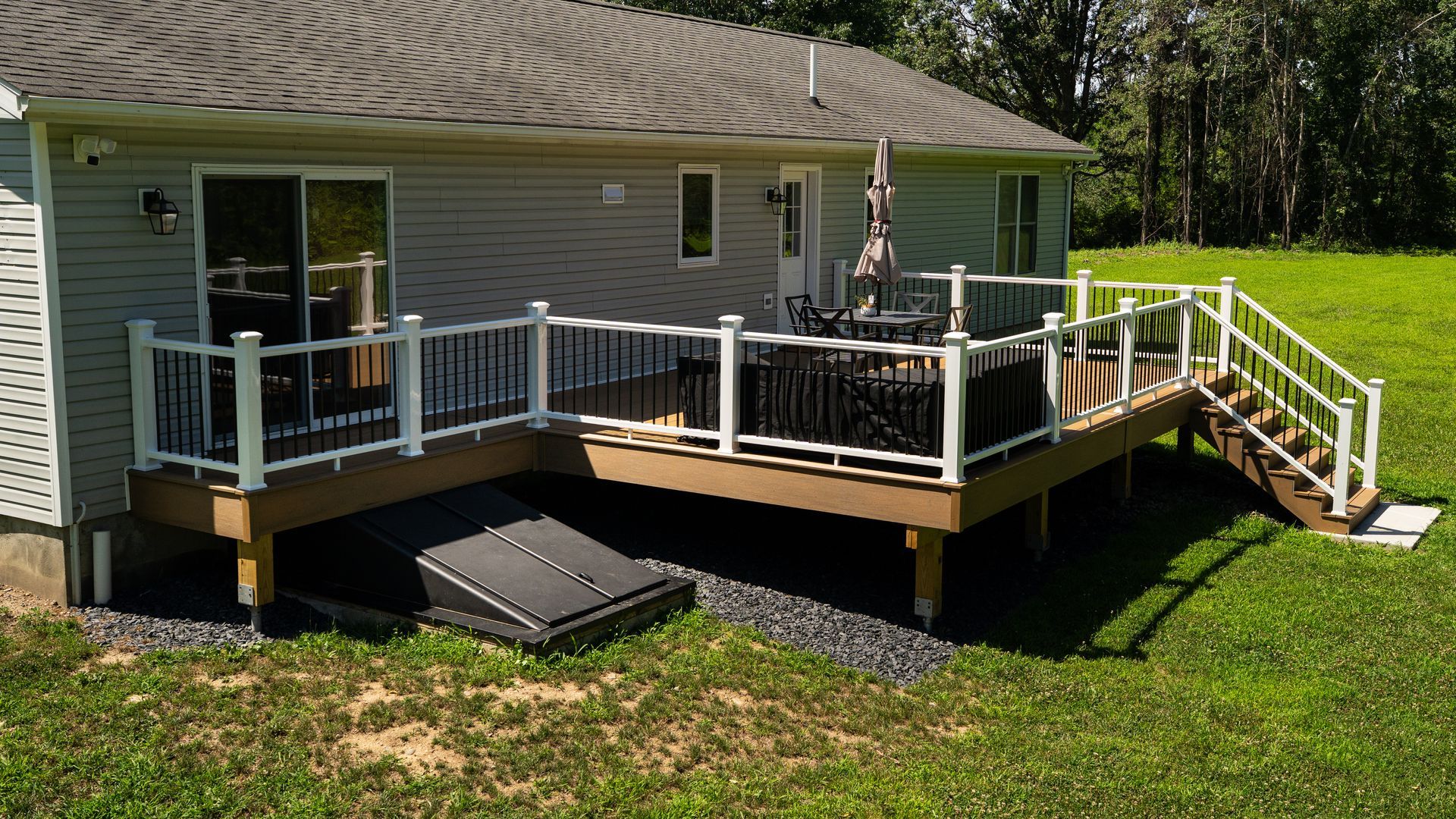 House with a wooden deck and white railing, stairs on the right, and a ramp on the left in a grassy yard.
