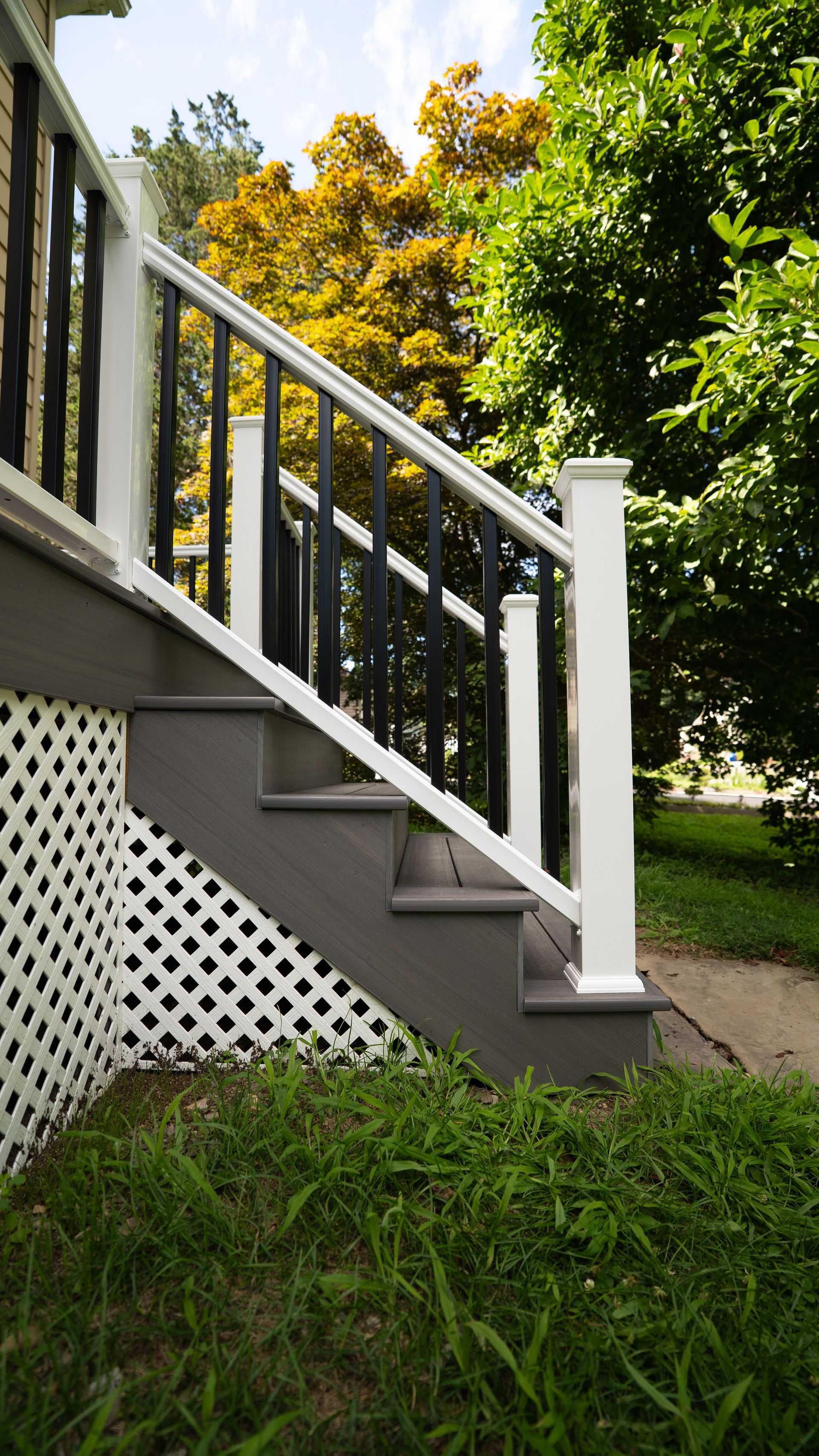 White porch stairs with lattice skirting beside green grass and trees in the yard