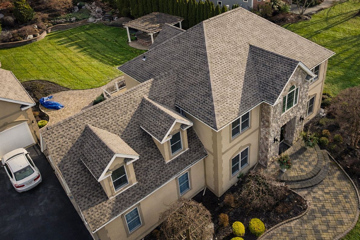 Aerial view of a large beige house with a gray roof, driveway, and landscaped yard.