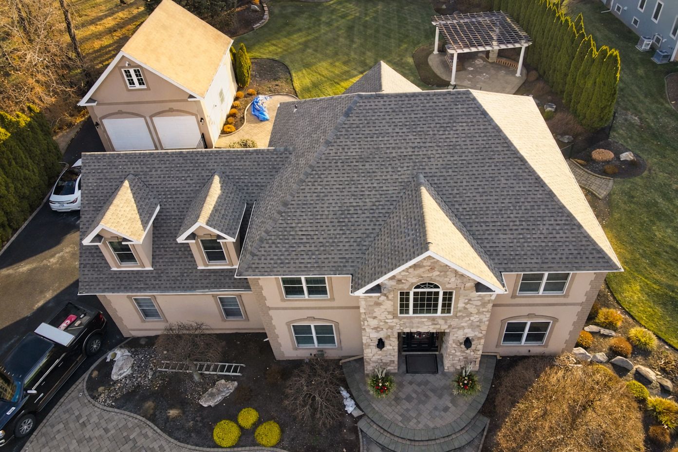 Aerial view of a large beige suburban house with a gray roof and landscaped front yard.