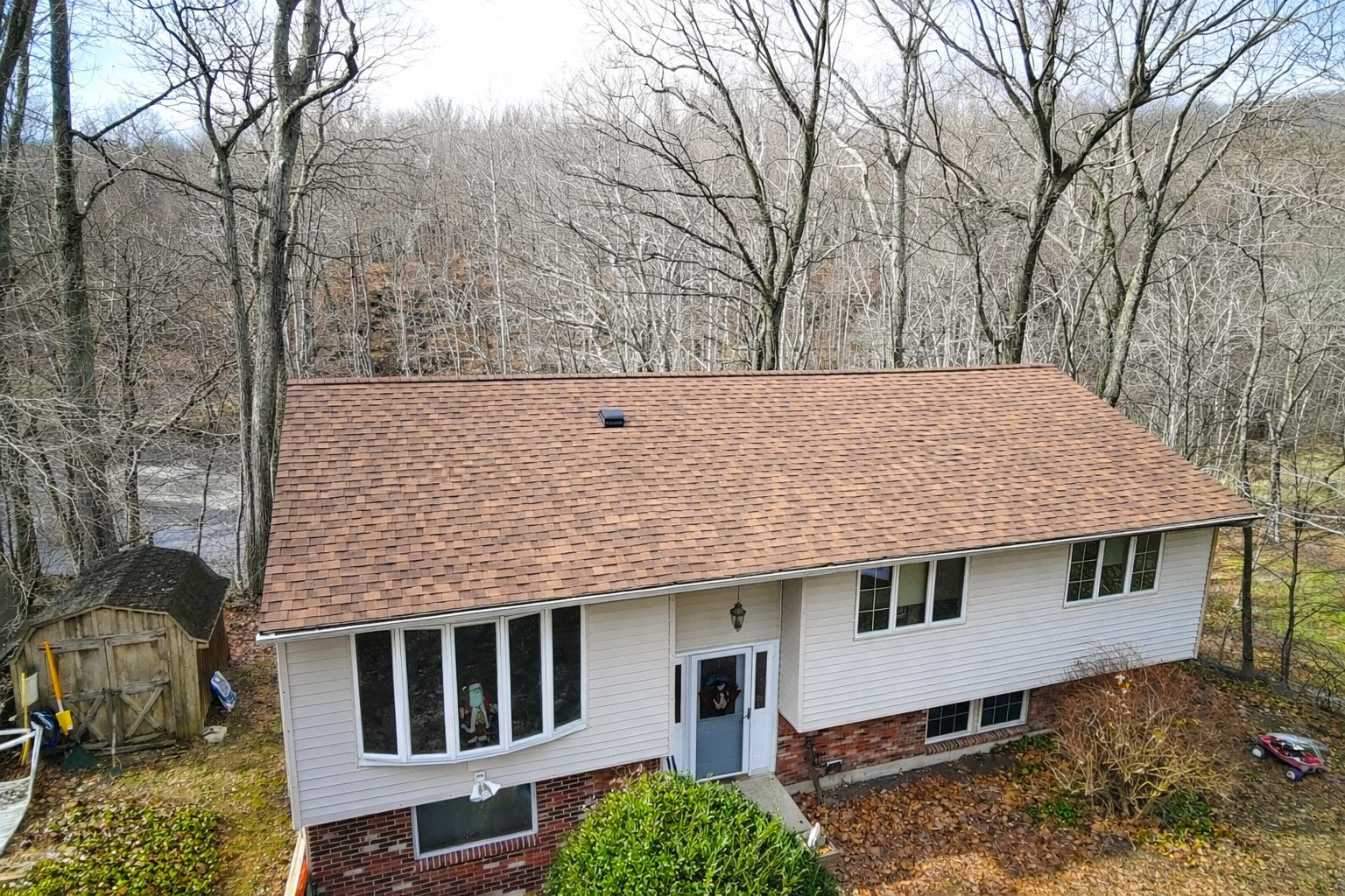 White house with brown roof surrounded by leafless trees in a wooded yard