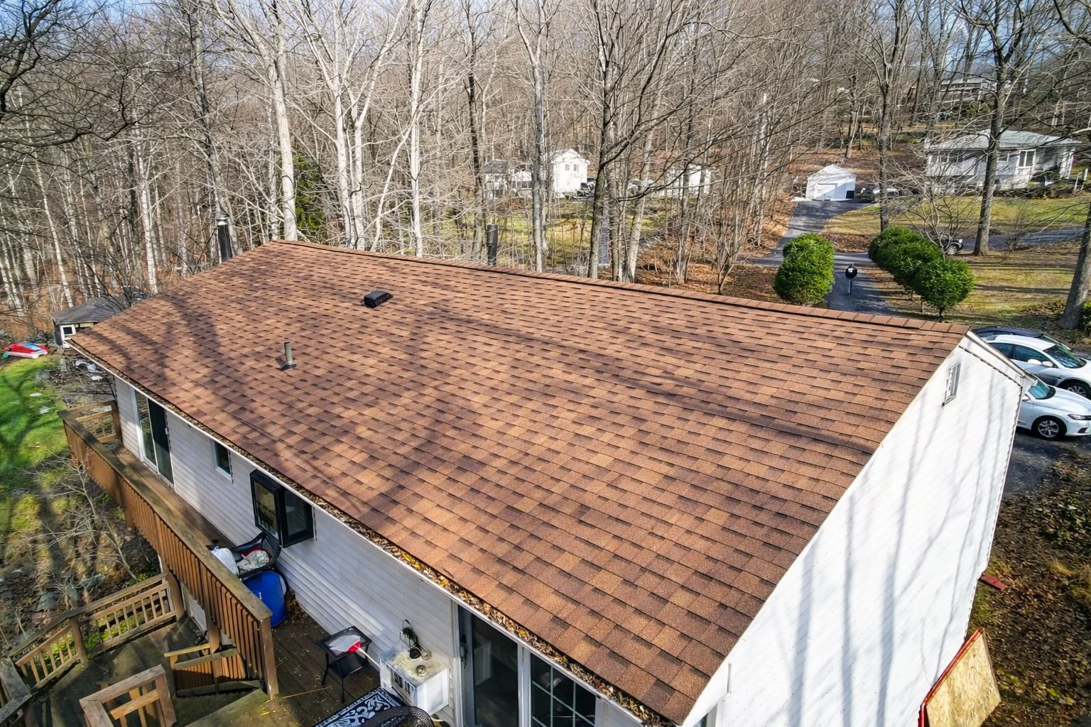 Aerial view of a house with a brown shingle roof in a wooded suburban area
