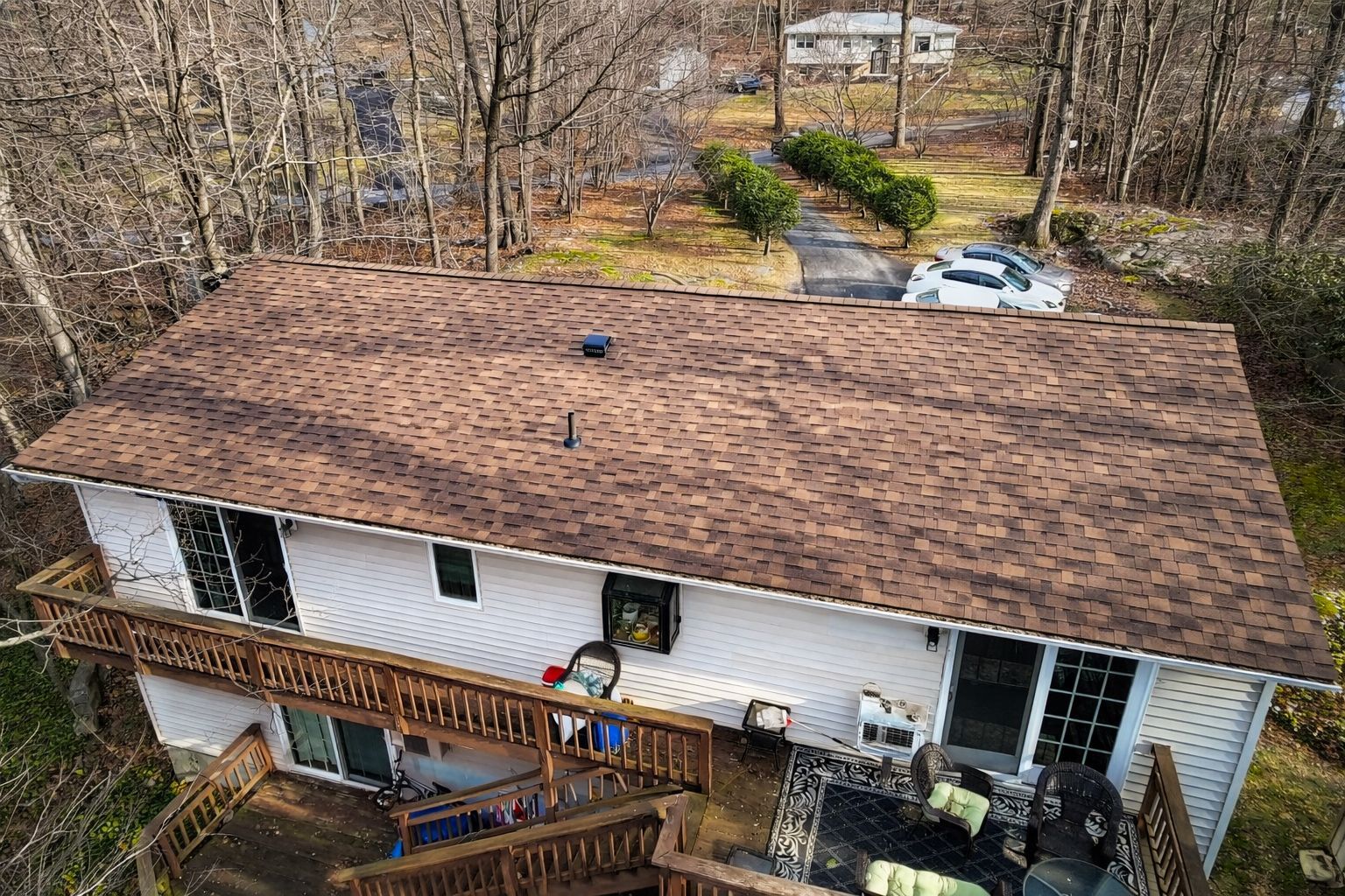 Aerial view of a white house with a brown roof and wooden deck beside leafless trees and parked cars