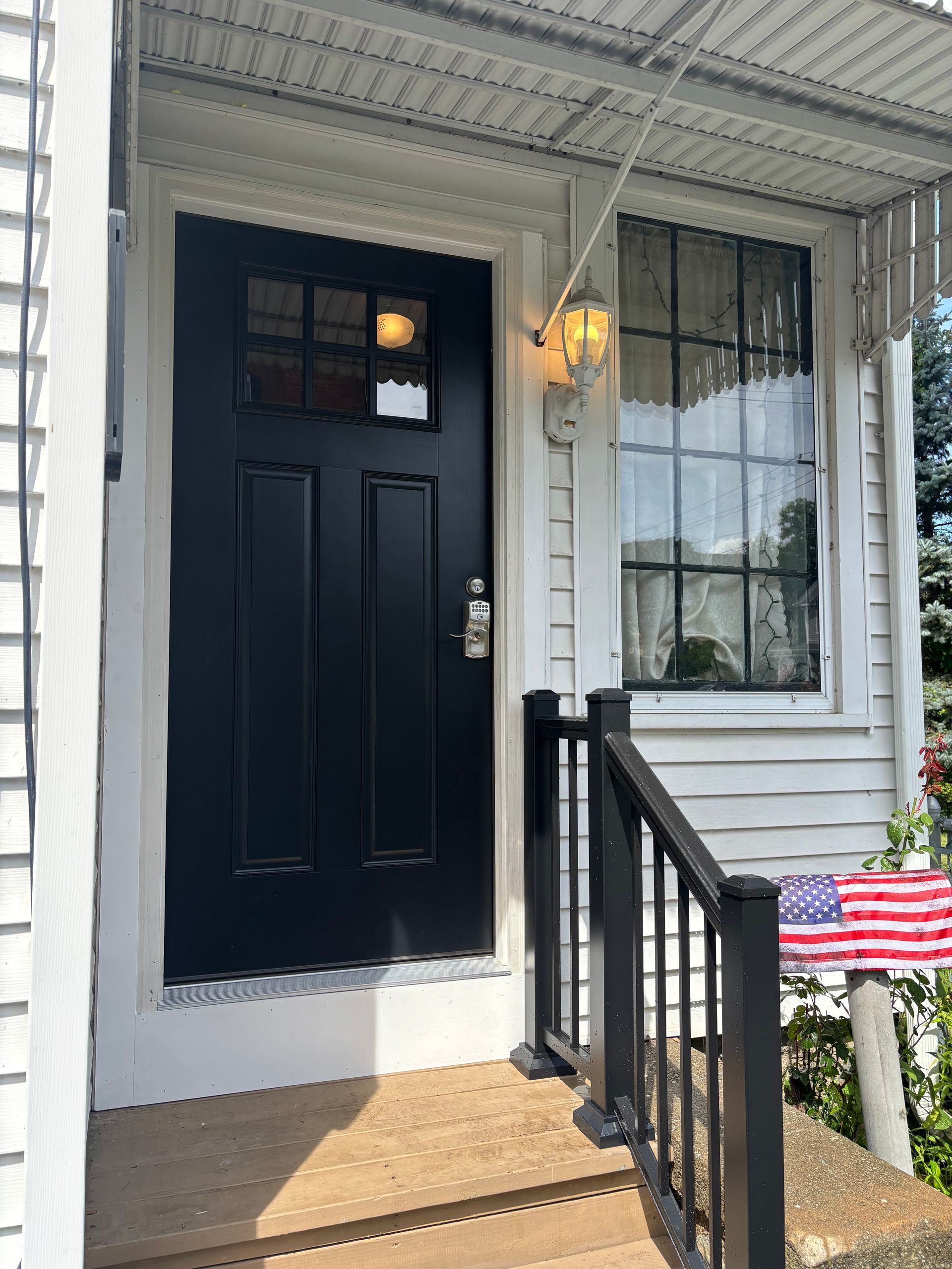 Front porch with a dark blue door, white siding, black railing, and an American flag decoration.