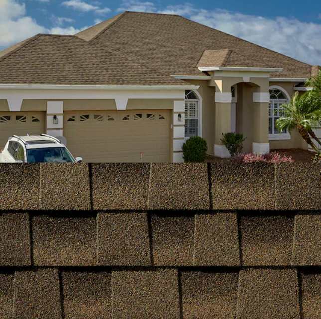 Suburban house with tan roof and garage, partially obscured by a brick wall in the foreground