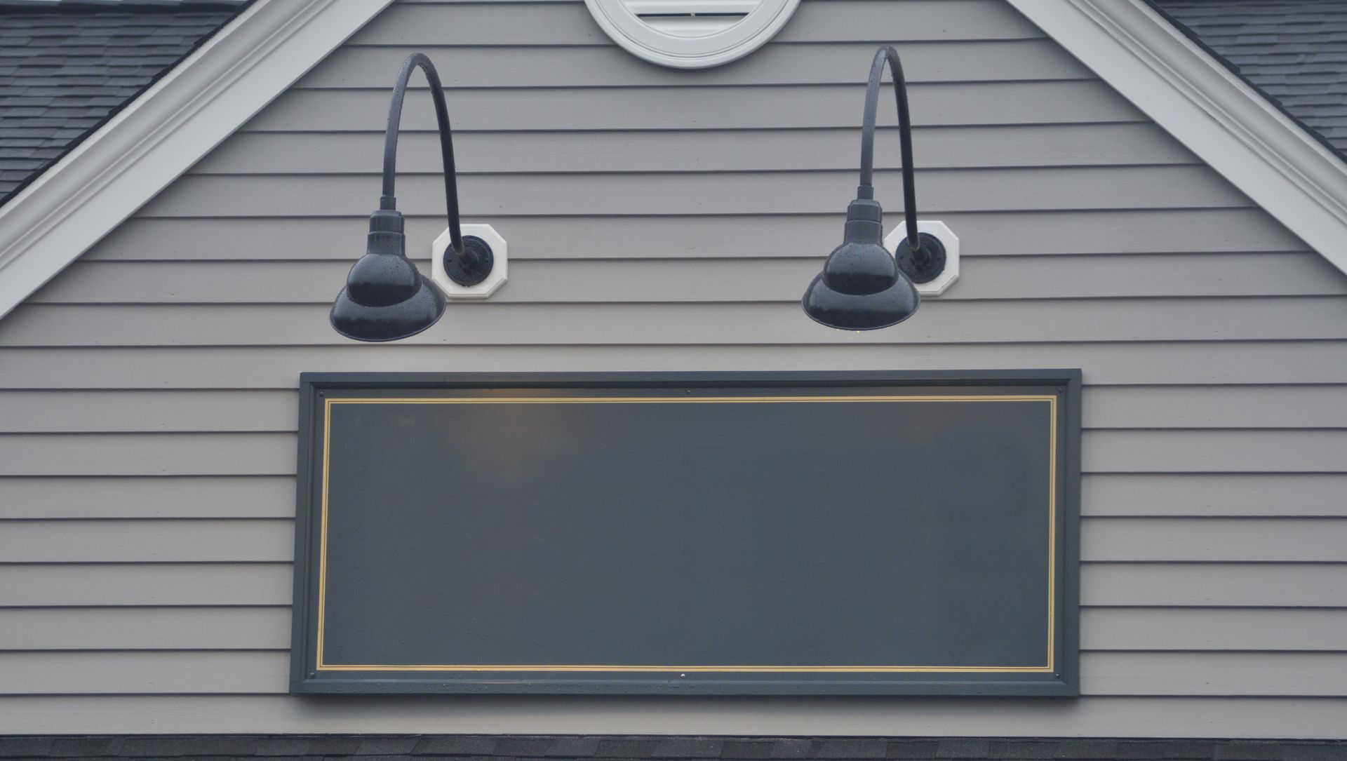 Gray house exterior with two black wall lights above a blank rectangular signboard