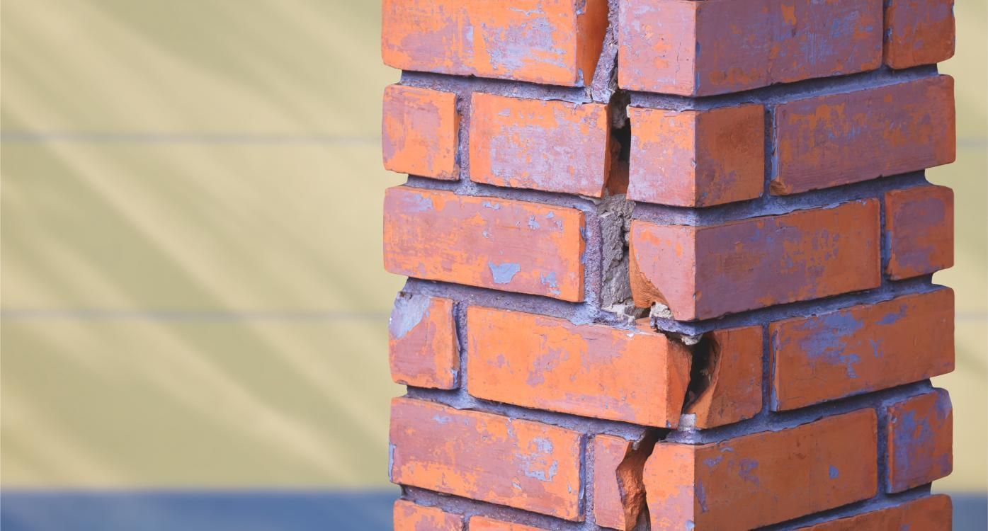 Damaged red brick pillar with a visible crack near the base against a blurred background